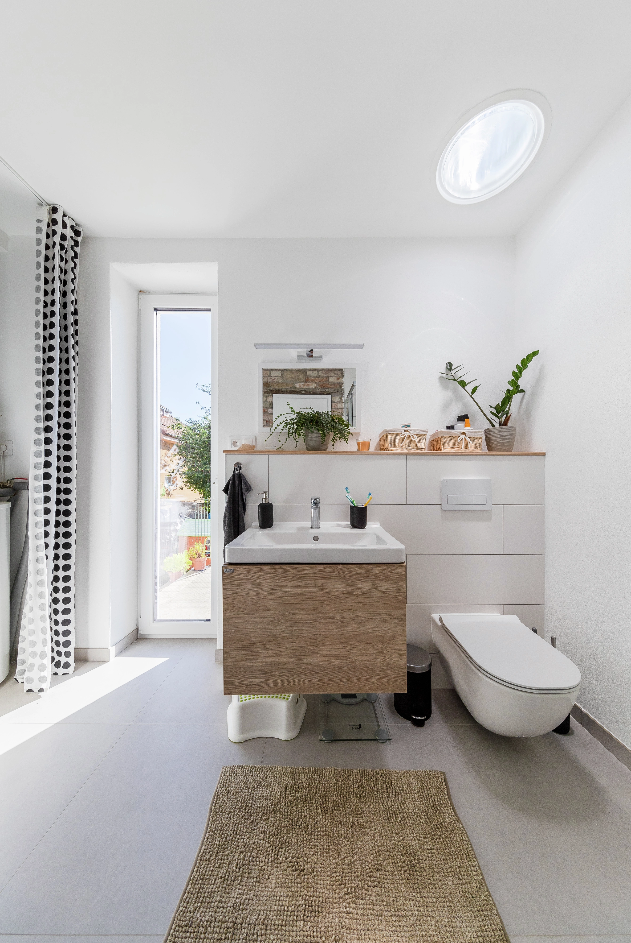 Modern fürdőszoba zuhanykabinnal, mennyezetbe épített VELUX fénycsatornával és nagyméretű üvegajtóval, amely bőséges természetes fényt enged be a helyiségbe