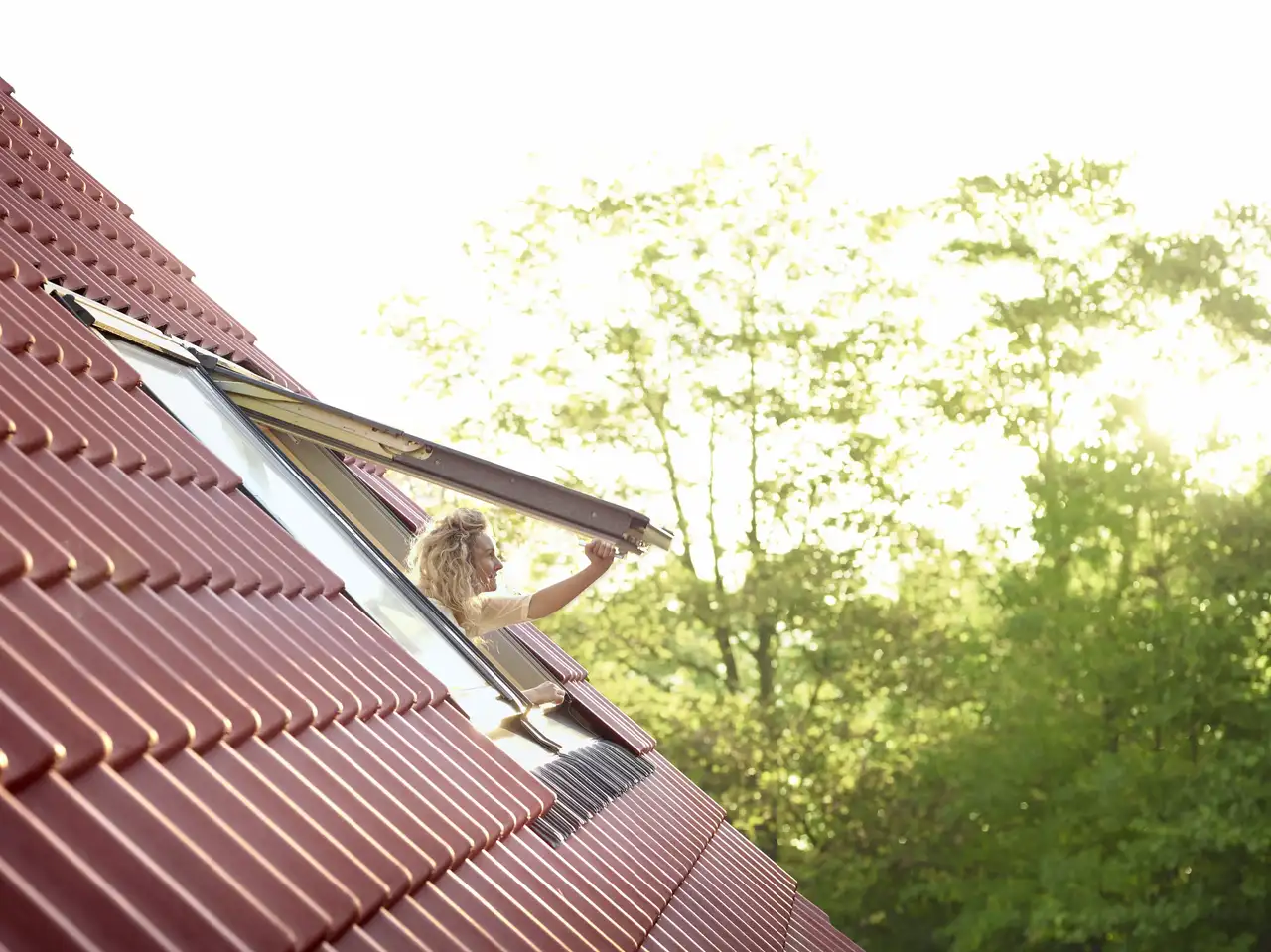Jeune femme ouvrant une fenêtre de toit VELUX sur un toit en tuiles