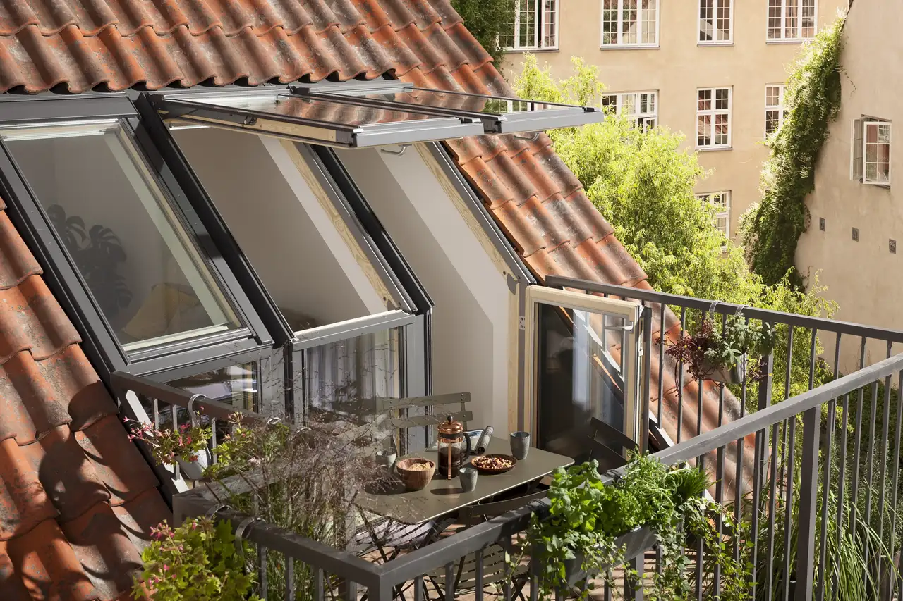 Begrünter VELUX Dachbalkon mit geöffneten Dachfenstern und kleinem Esstisch | VELUX Magazin