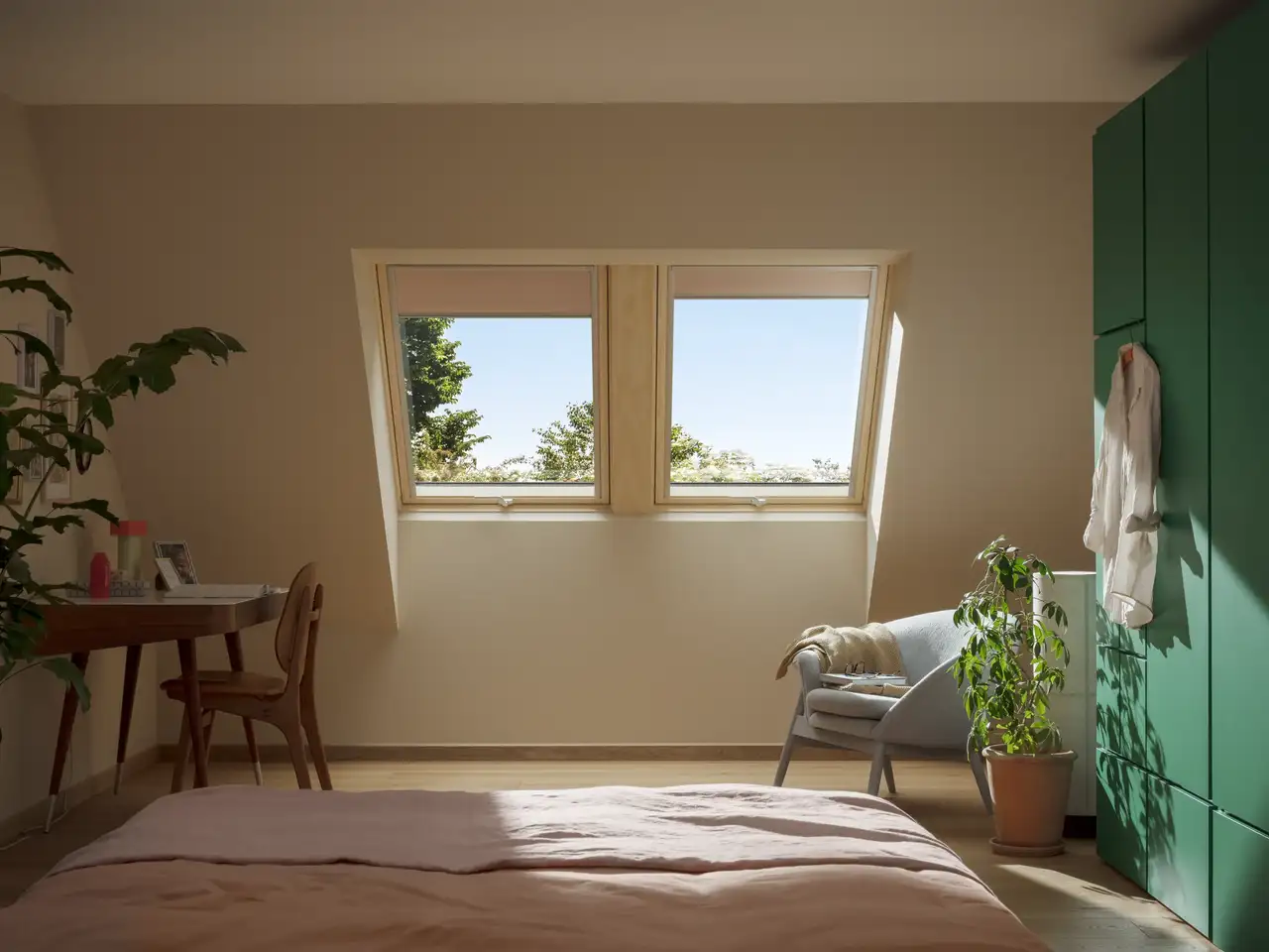 Attic bedroom with sloped ceiling and VELUX roof window and VELUX blinds, natural light and view to the outside.