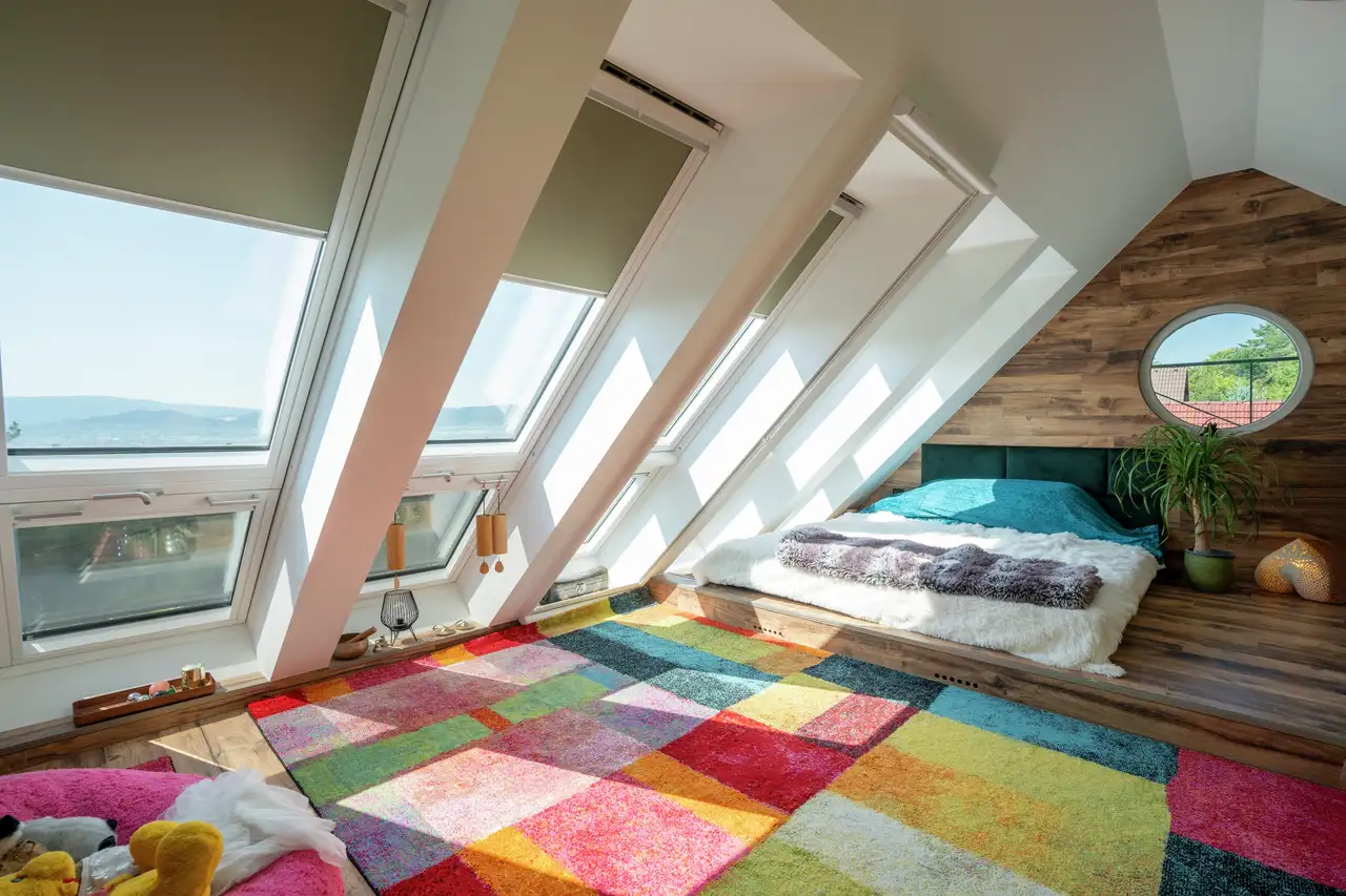 Chambre mansardée lumineuse avec fenêtres de toit VELUX, murs en bois clair et tapis coloré illustrant le style Dopamine decor 