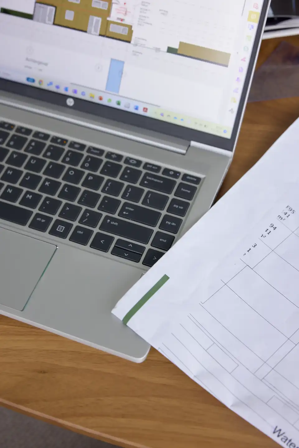 Notebook zobrazujúci architektonické plány vedľa tlačených technických výkresov, zdôrazňujúci podrobné plánovanie projektu renovácie.