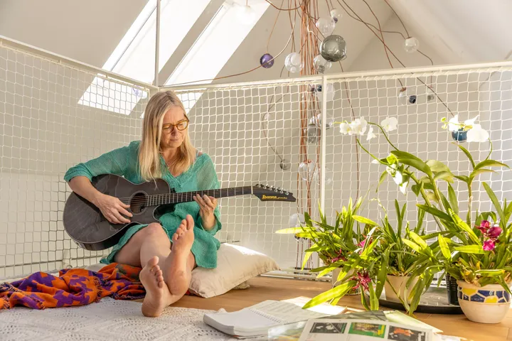 Gemütliches Dachboden-Zimmer mit Person, die unter einem VELUX-Fenster Gitarre spielt, umgeben von üppigen Pflanzen.
