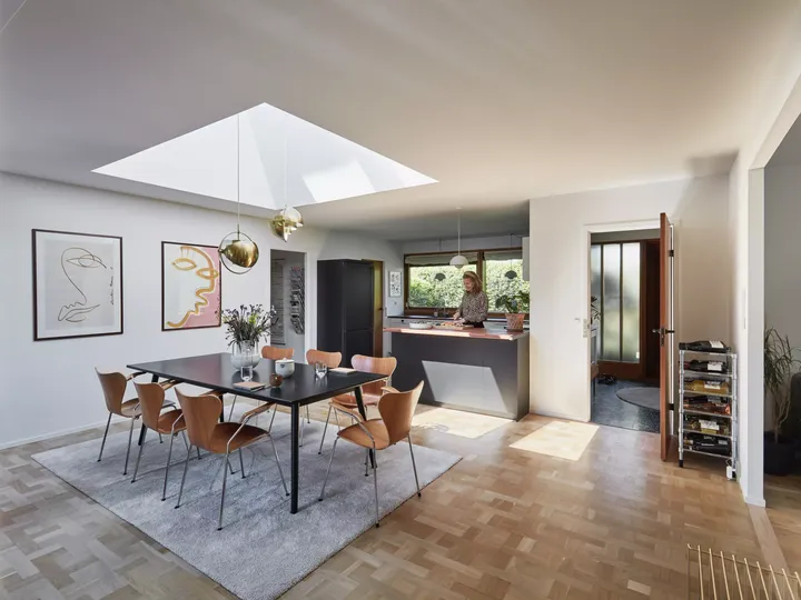 Moderne Küche mit Essbereich unter einem VELUX Dachflächenfenster, hölzernem Boden und goldenen Akzenten.