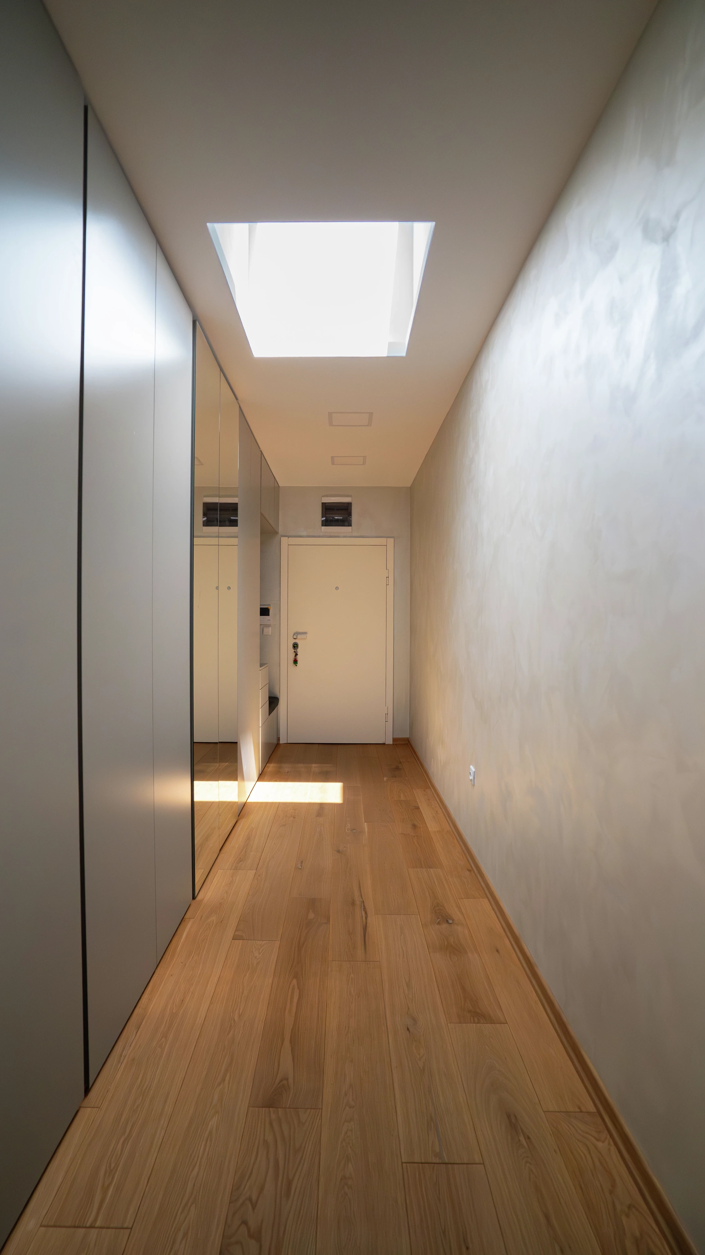 Narrow modern hallway lit by a VELUX flat roof window above wooden flooring.