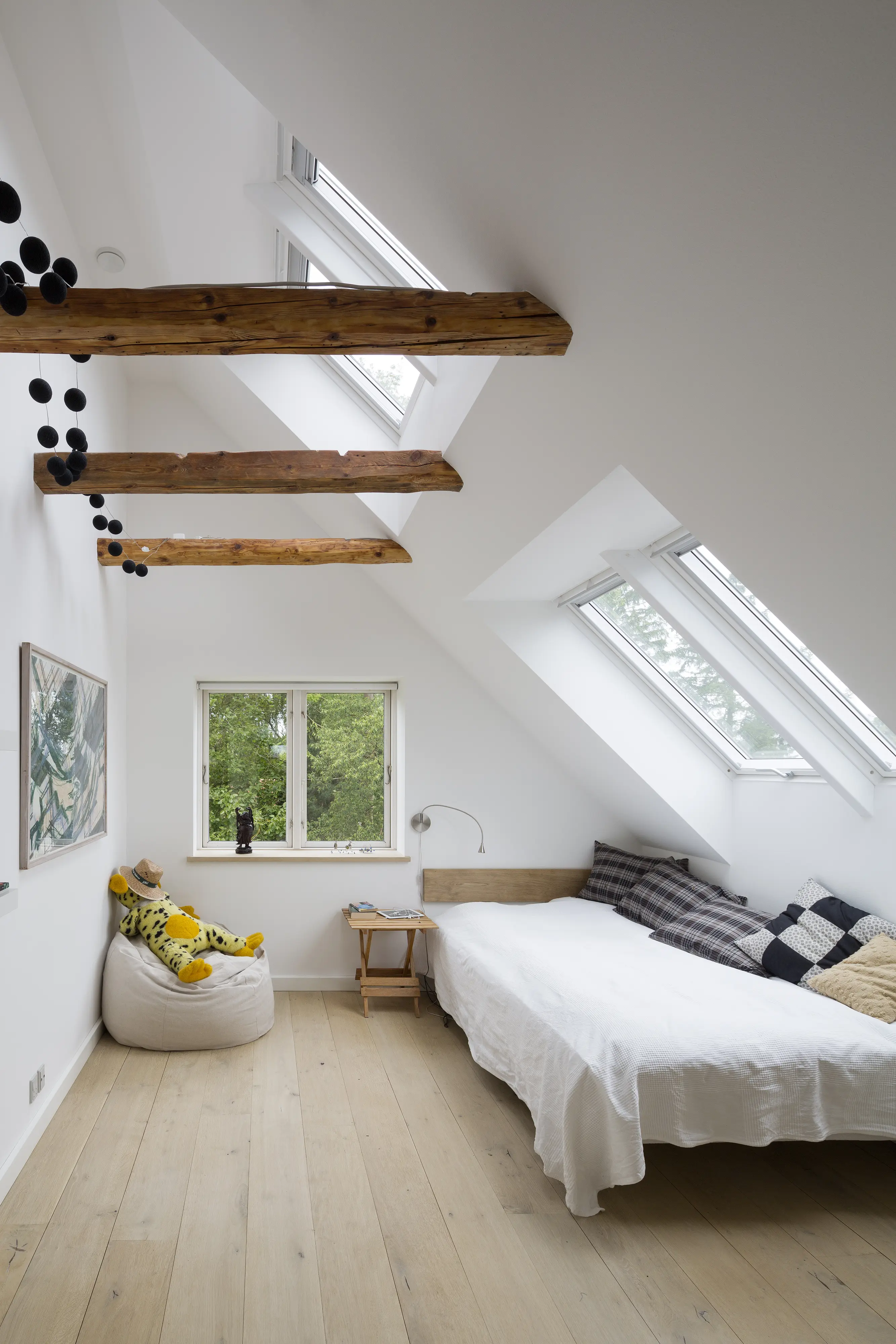 Dormitor la mansardă cu tavan înclinat, ferestre VELUX și grinzi aparente.