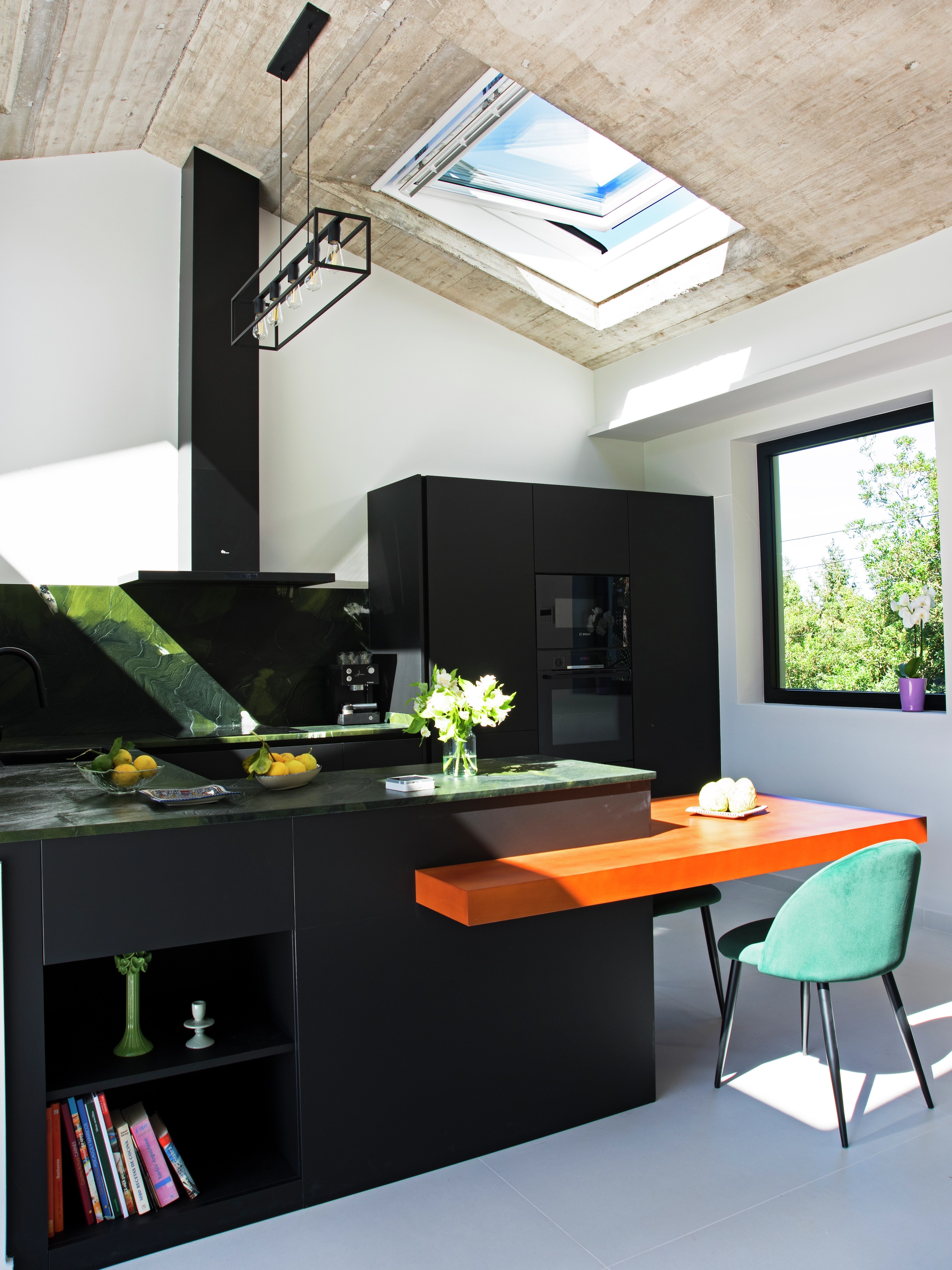 Cocina con tejado inclinado iluminada por ventanas verticales y ventanas de tejado abierta para una correcta ventilación.