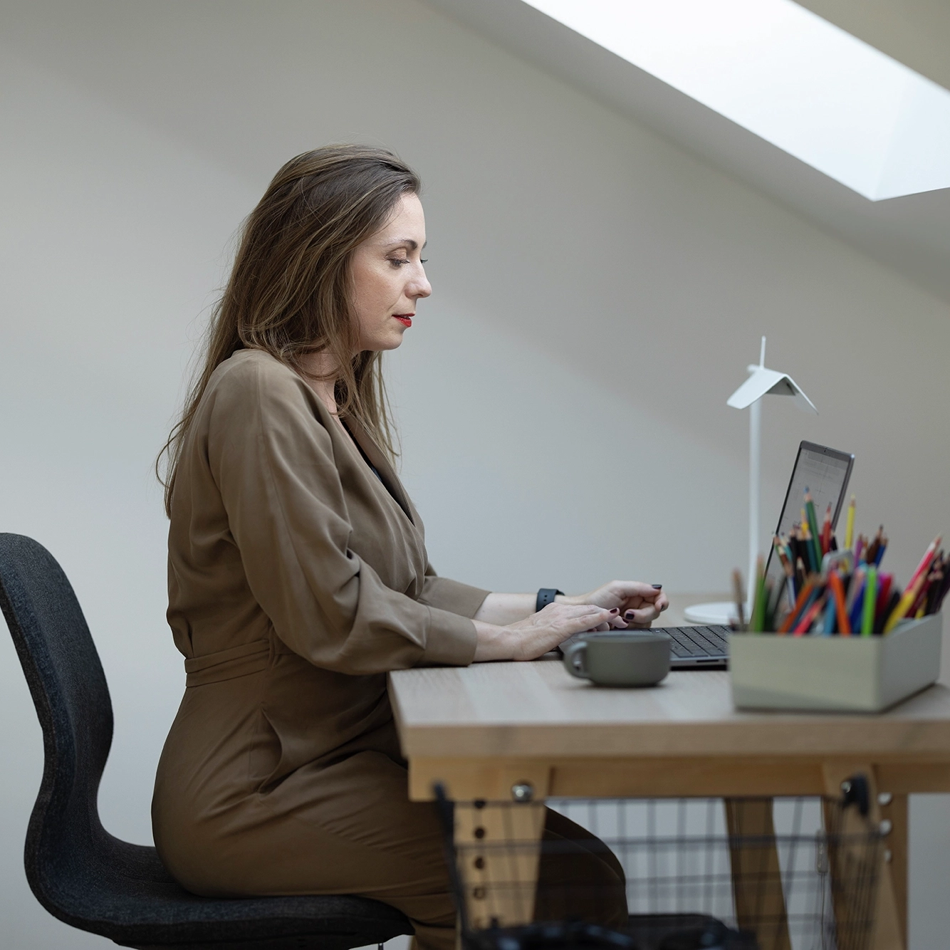 Donna al computer in ufficio domestico in mansarda con soffitto spiovente e finestra per tetti VELUX.