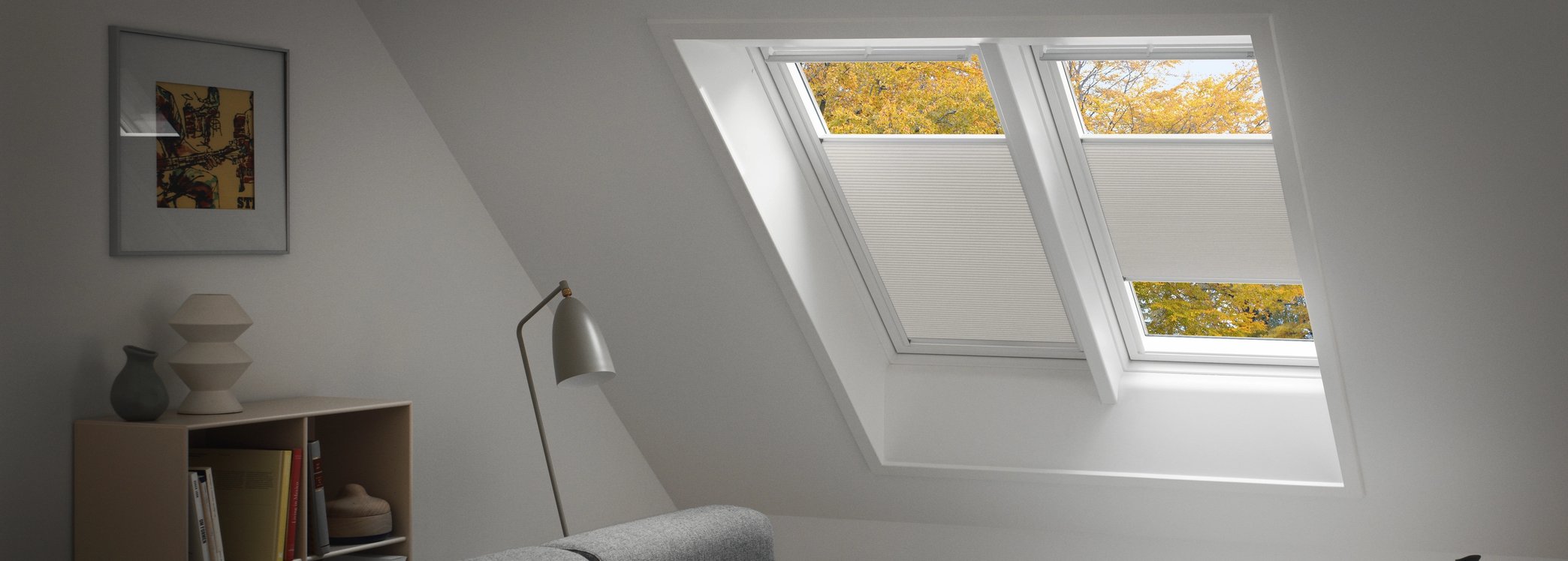 Attic living room with VELUX roof windows and blinds partly lowered over a large grey sofa.