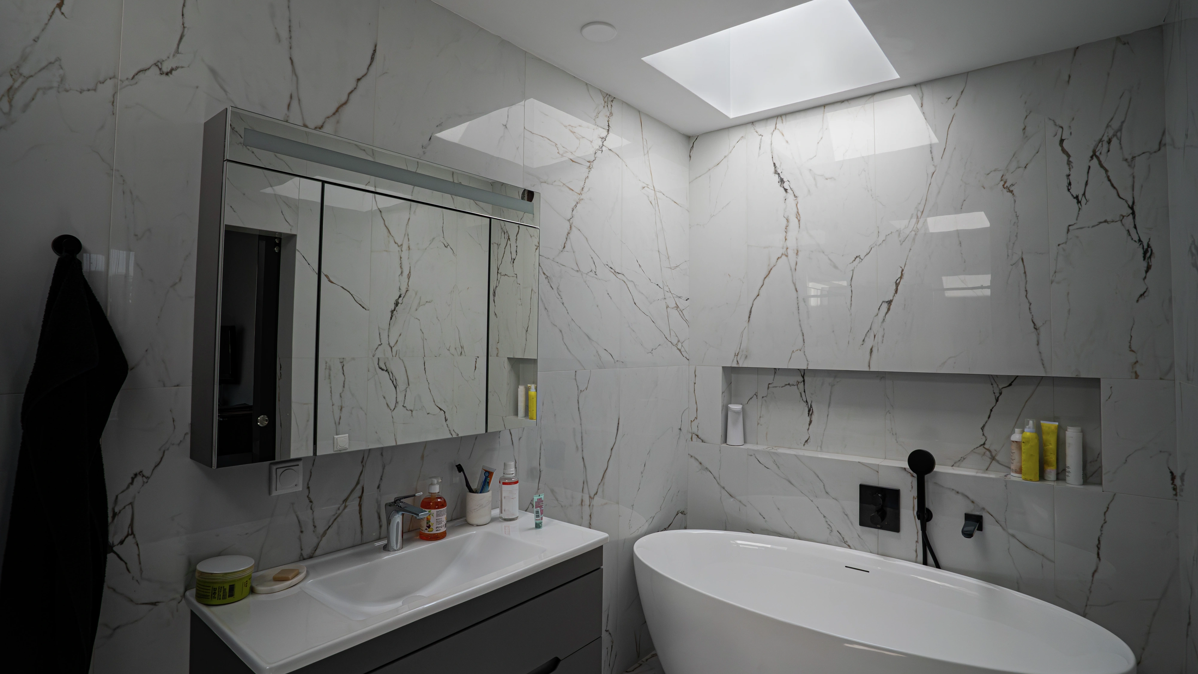 Modern marble bathroom lit by VELUX flat roof window above freestanding bathtub.