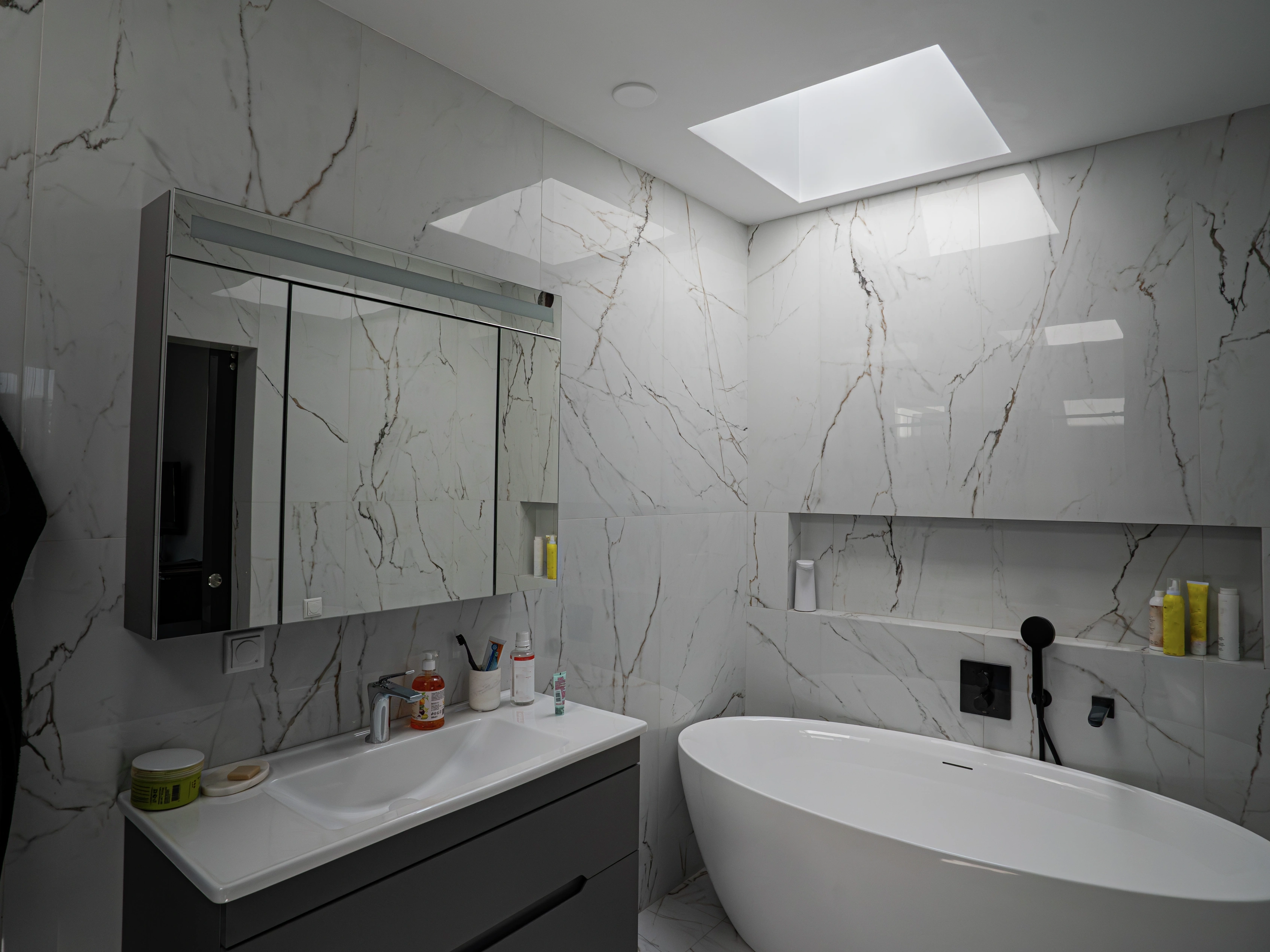 Modern marble bathroom lit by VELUX flat roof window above freestanding bathtub.