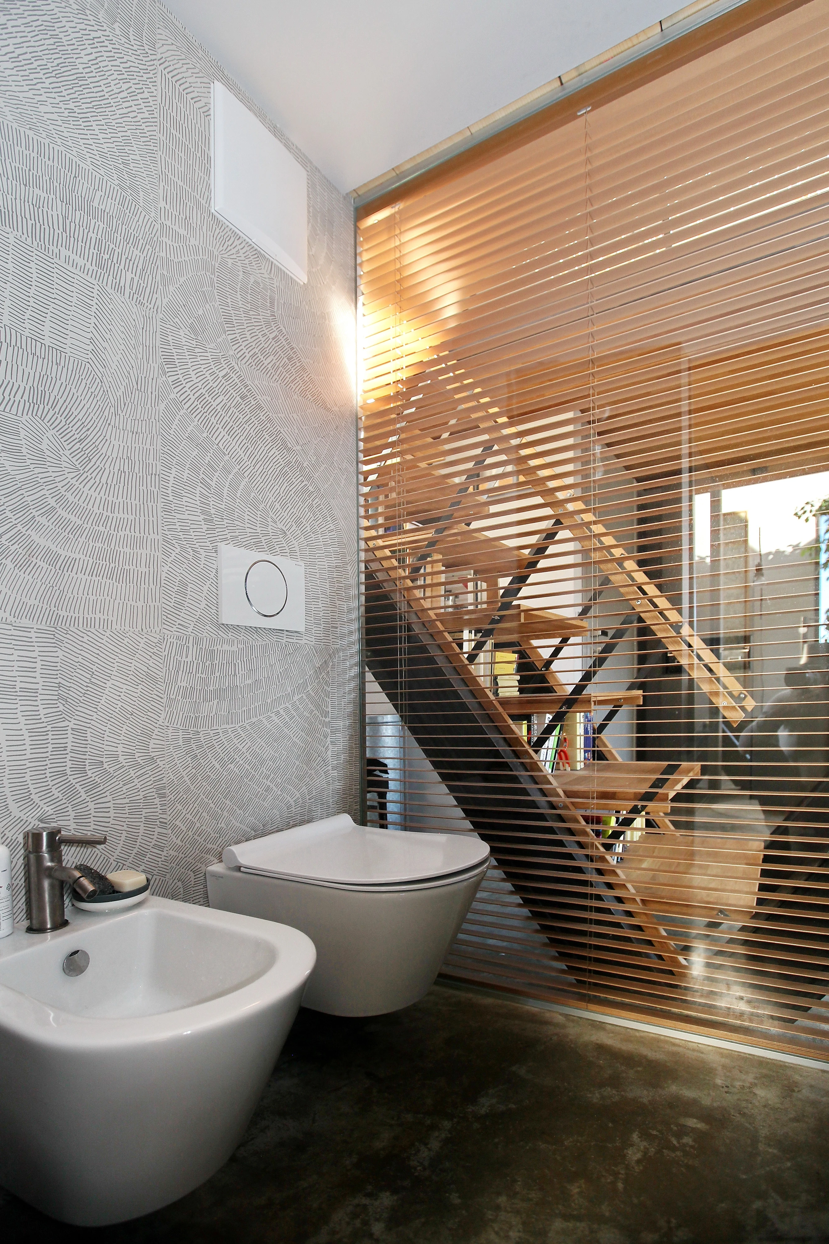 Modern bathroom with bidet, toilet, and view of staircase through blinds.