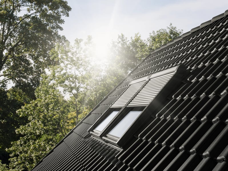 Roof with black tiles and closed VELUX roof windows with electric shutters.