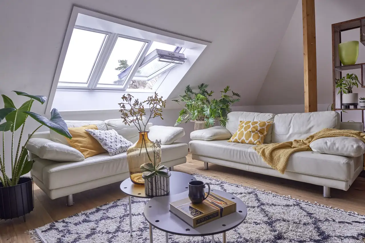 Séjour mansardé avec fenêtres de toit VELUX, nombreuses plantes vertes et mobilier dans des tons naturels ponctués d’accents jaunes 