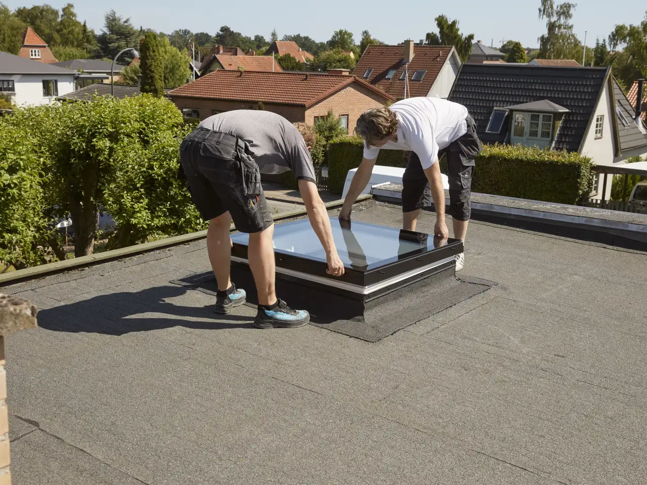 deux installateurs terminent la pose d'une fenêtre pour toit plat VELUX