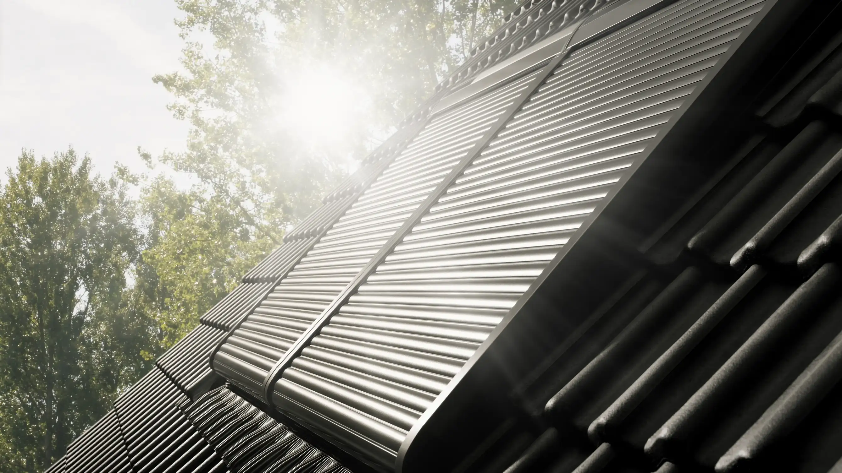 Sloped roof with black tiles and VELUX roof window and VELUX roller shutter.