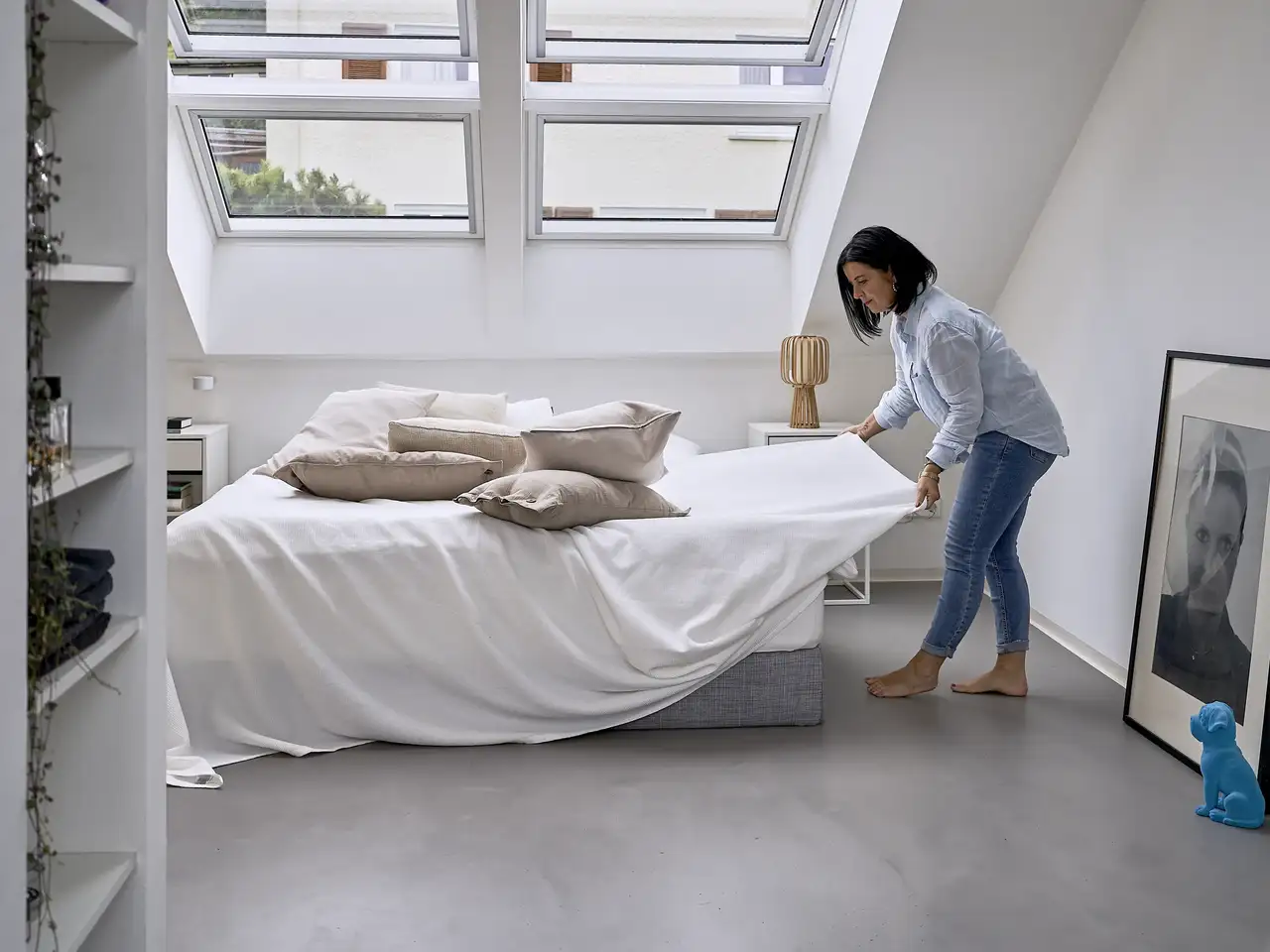 Donna che rifà il letto sotto grandi lucernari | Rivista VELUX