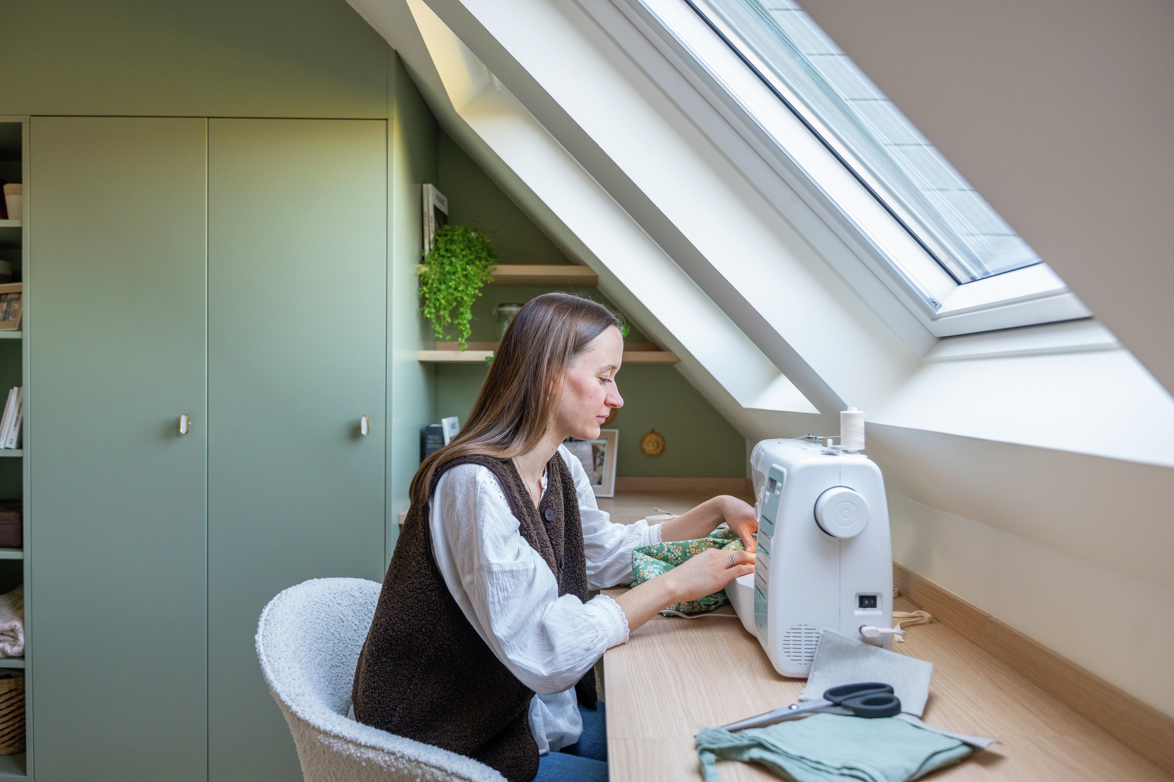 Femme assise à son bureau, en train de coudre face aux fenêtres de toit