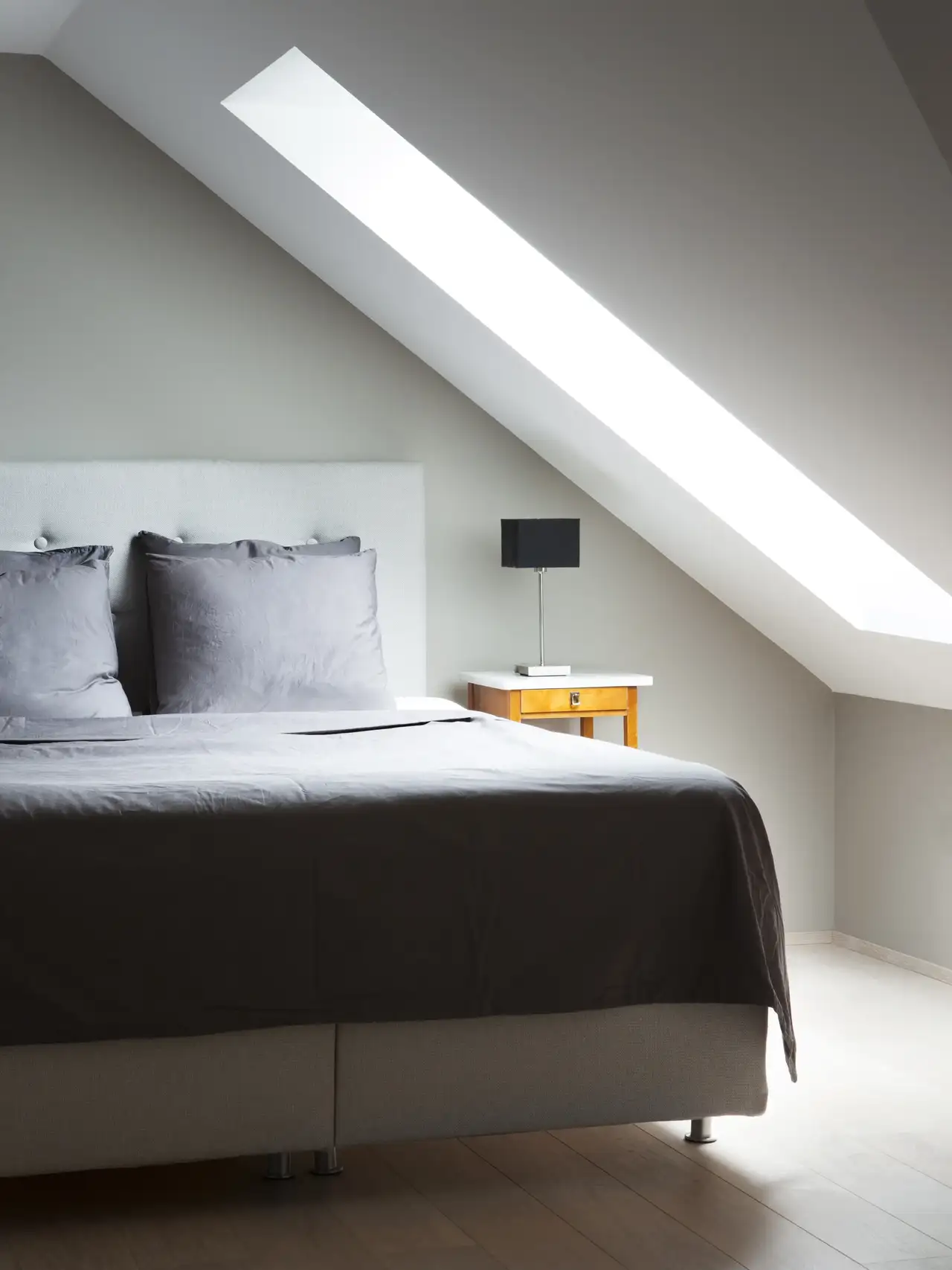 Chambre sous les combles de style minimaliste avec lit double, table de chevet et petite lampe. 