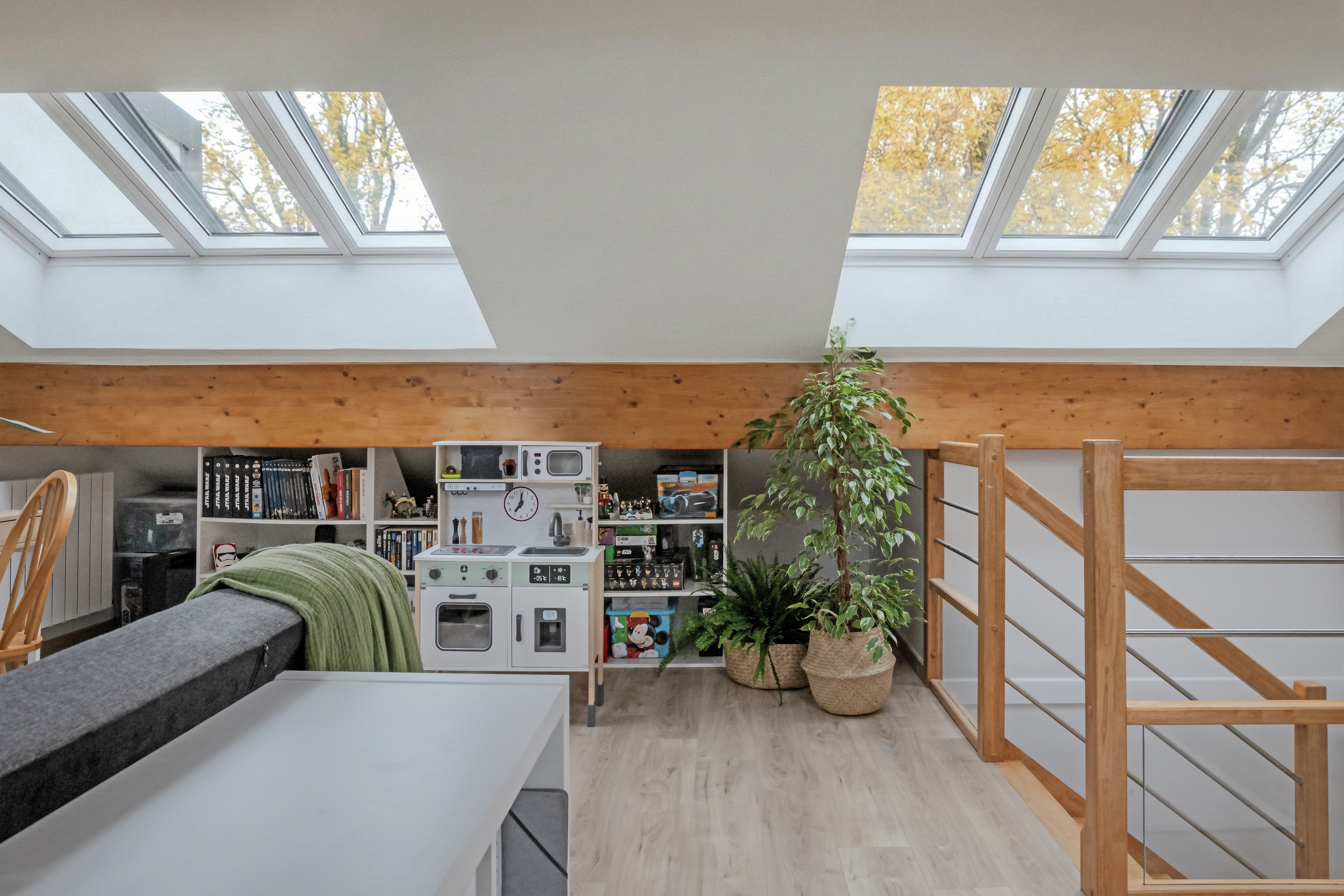 Attic playroom with sloped ceiling and VELUX roof windows, play kitchen and bookshelves.
