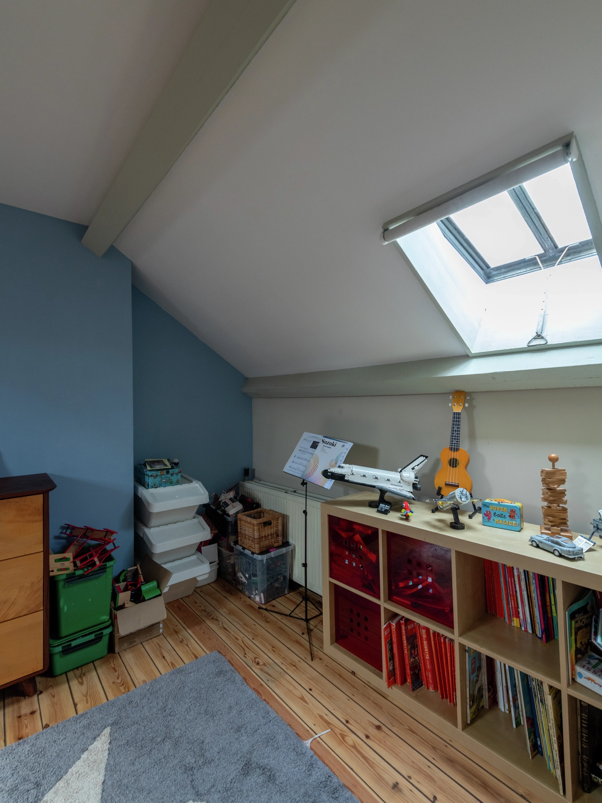 Vue d’une chambre mansardée pour enfants avec parquet bois et fenêtre de toit ancienne.