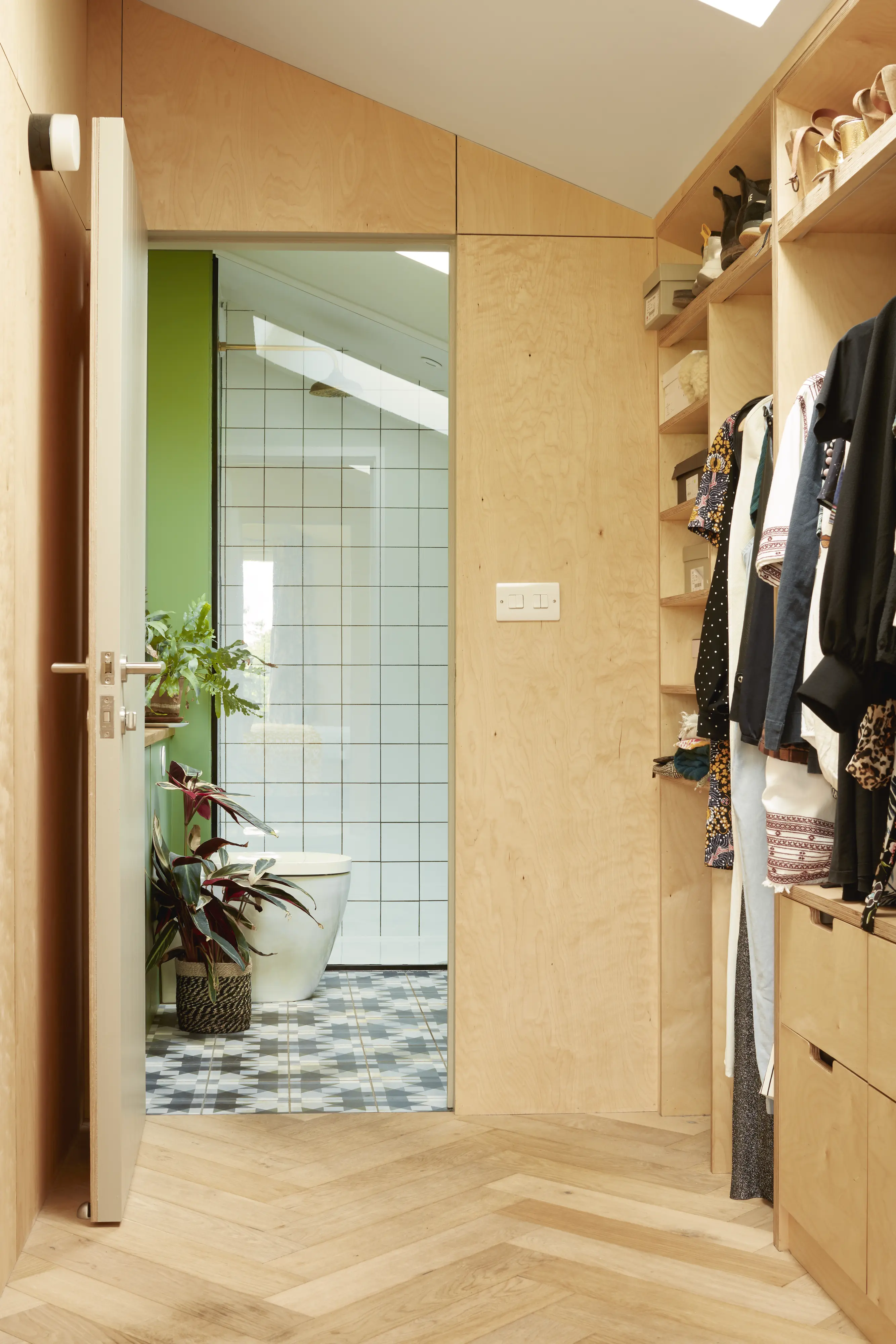 Walk-in closet with wooden shelves leading to a modern bathroom with VELUX roof window.