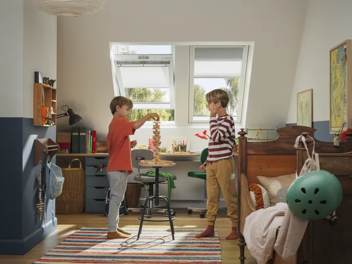 Zwei Jungs spielen Jenga unter Lichteinfall der zwei geöffneten Dachfenster mit Sonnenschutz | VELUX Magazin