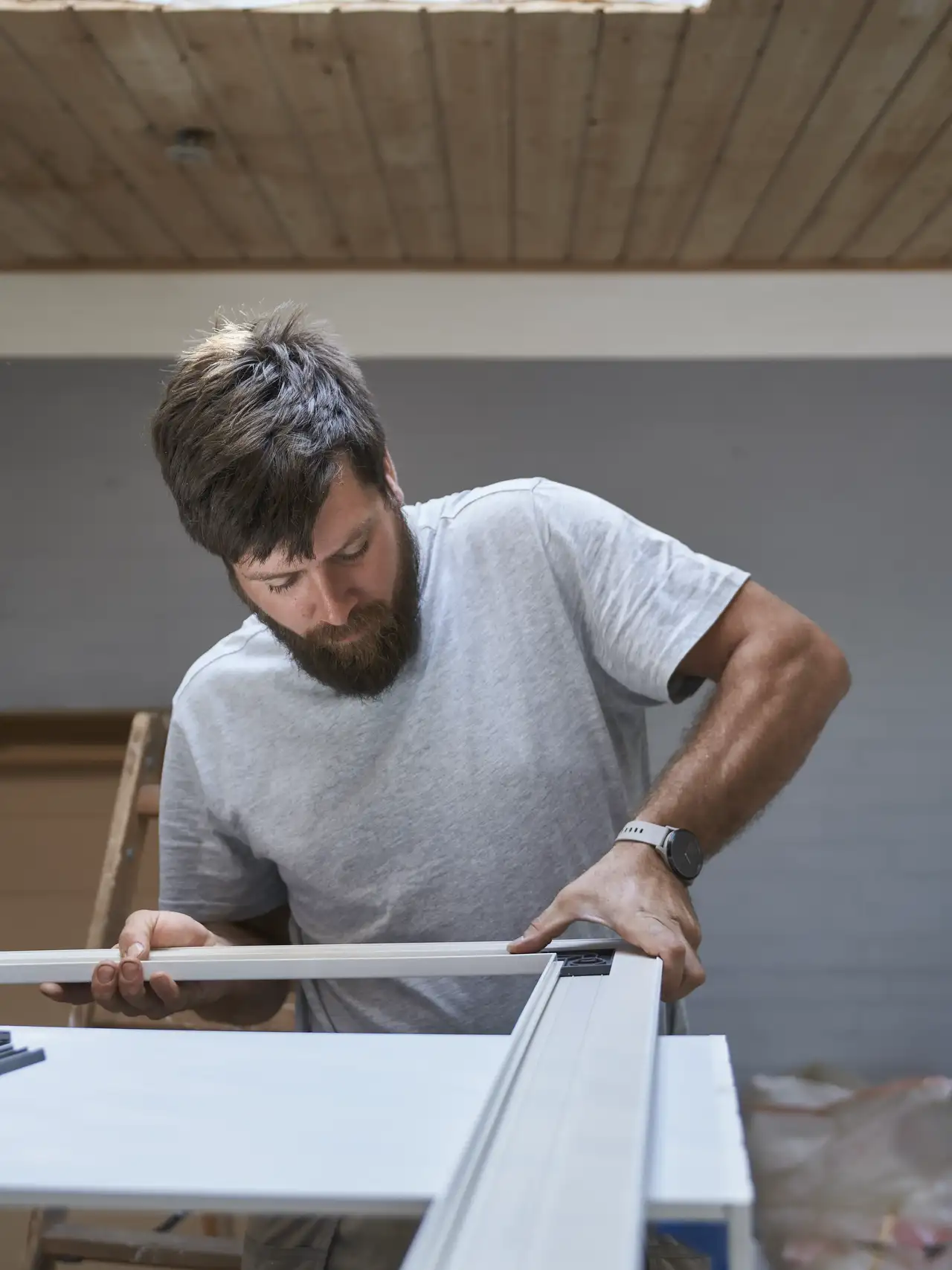 Man assembling a window frame under a wooden ceiling. 