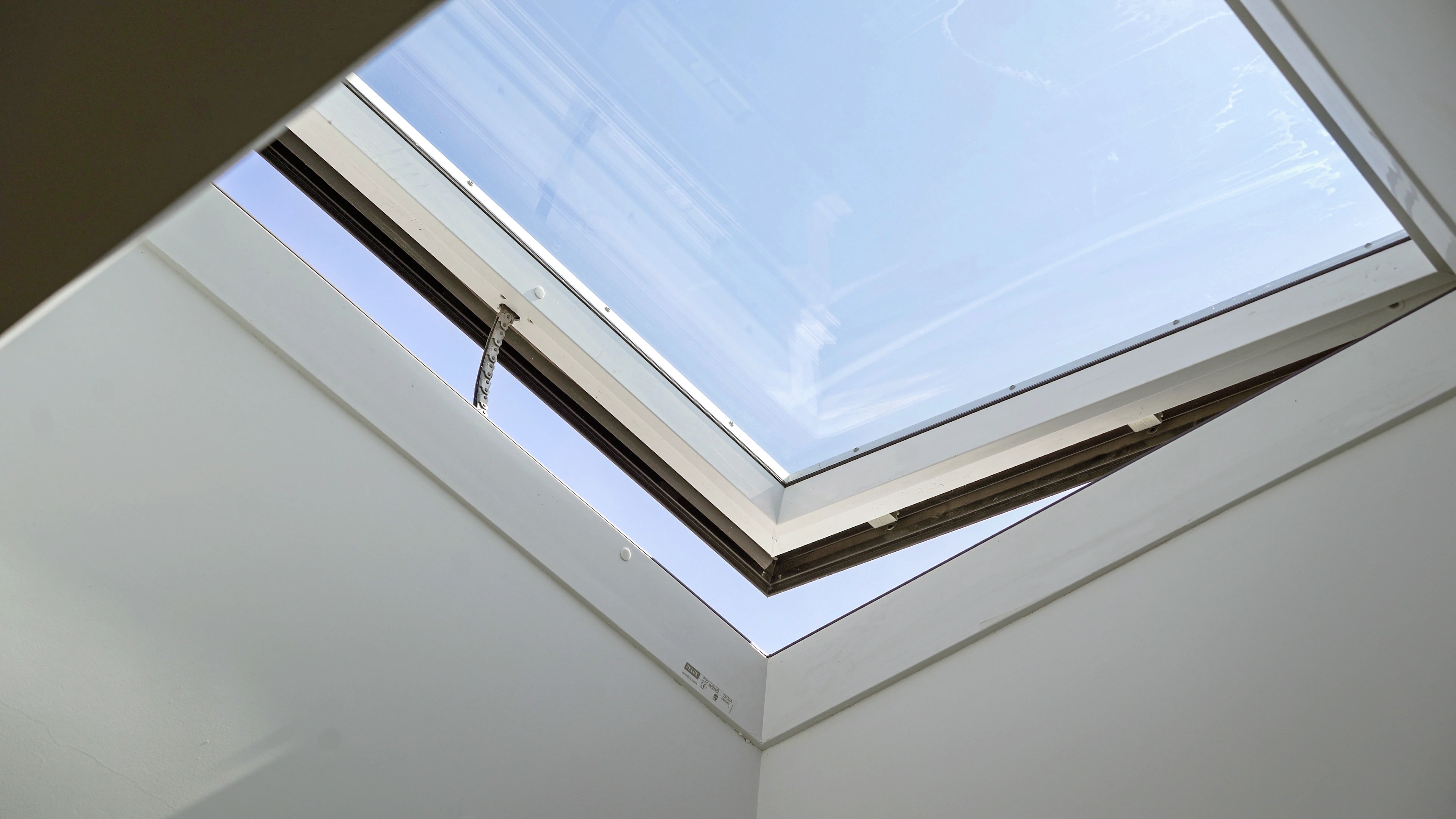 Partly open VELUX flat roof window bringing daylight into a white room