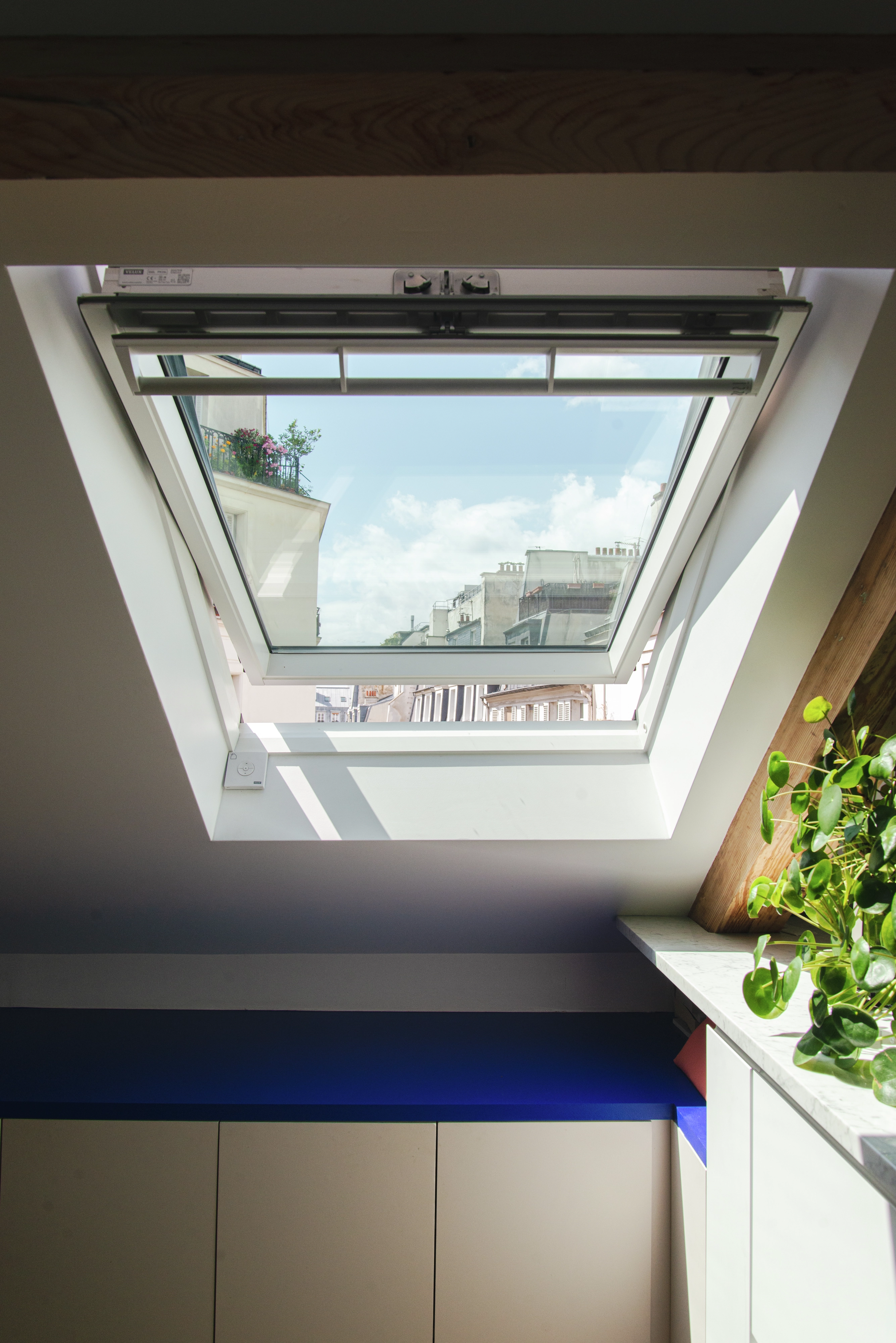 Espace de comble confortable avec une fenêtre de toit VELUX ouverte révélant le paysage urbain.