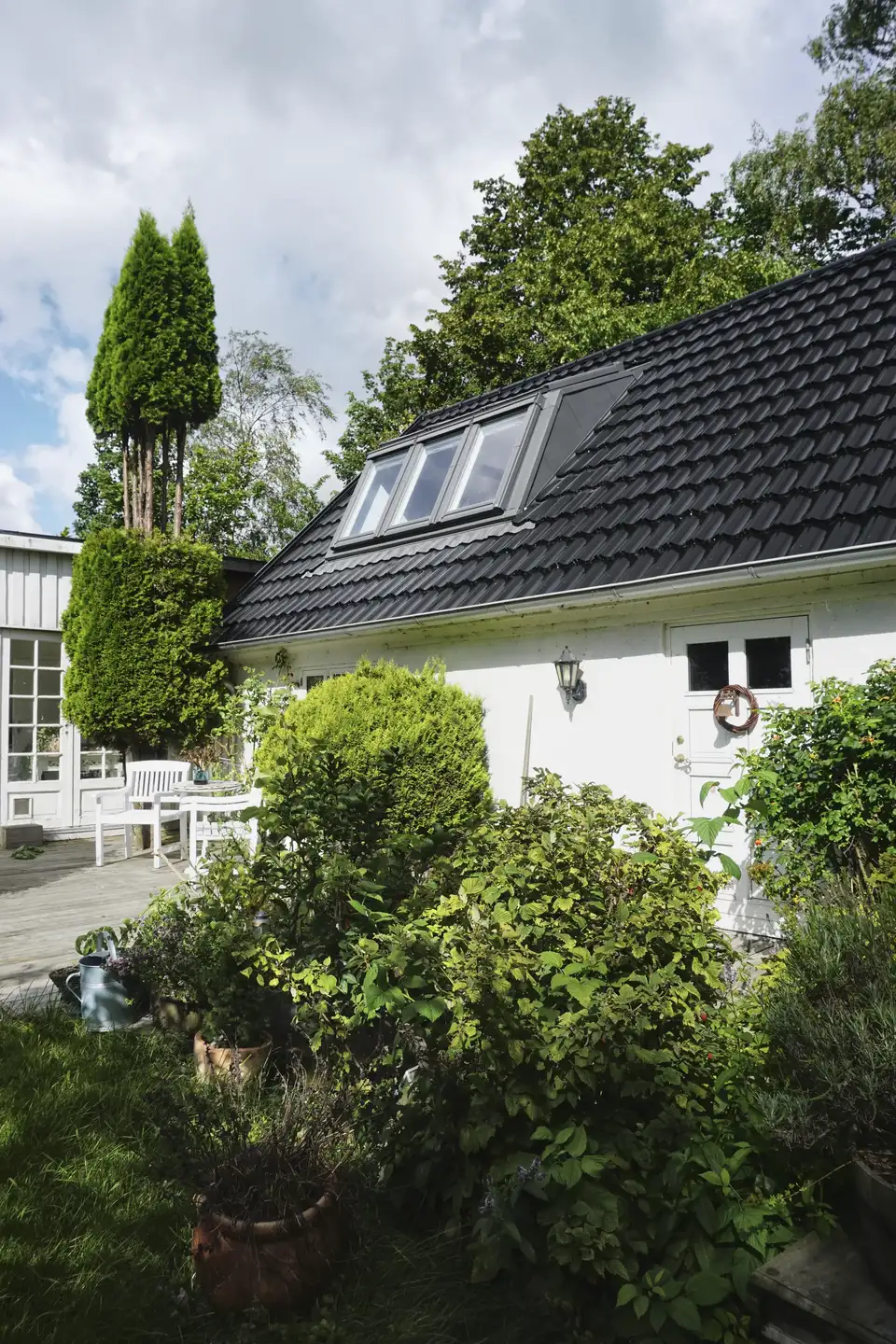 maison blanche avec tuiles noires et verrière 3en1 VELUX, entourée de végétation dense