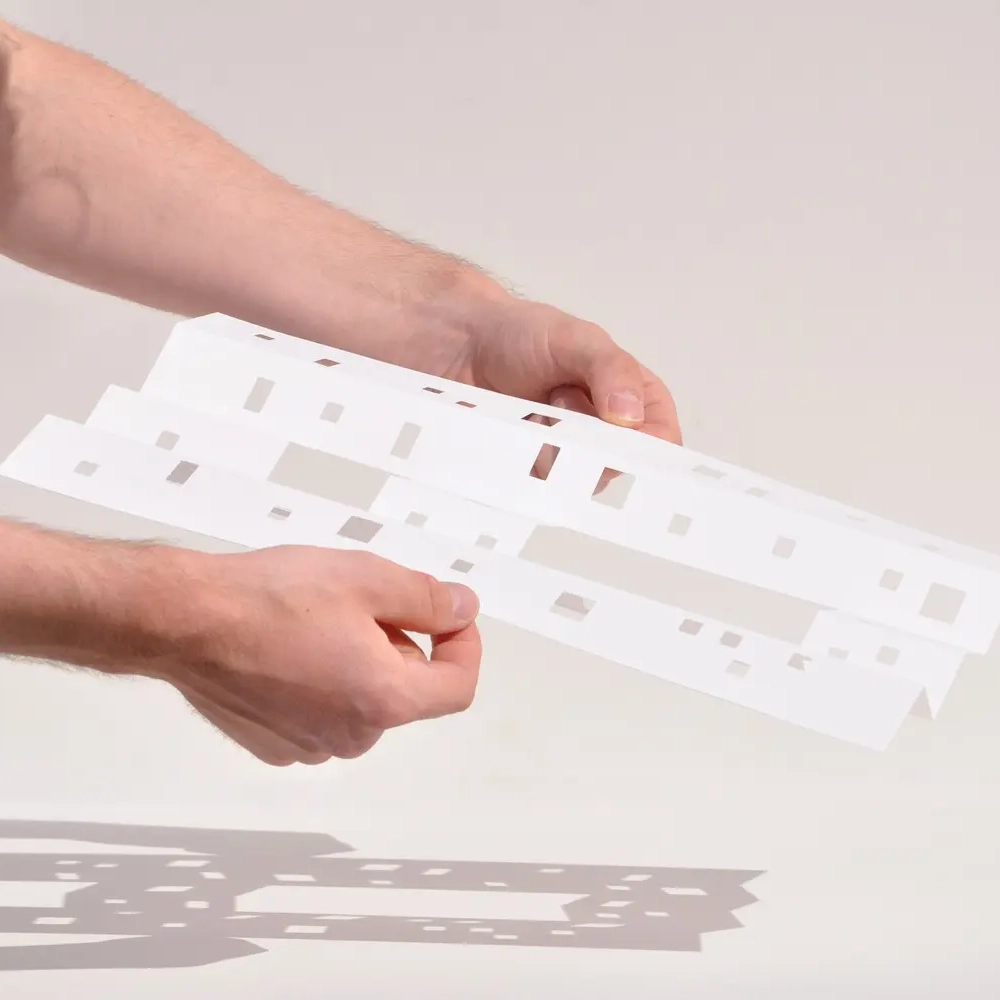 Hands holding a white paper model with intricate cutouts.