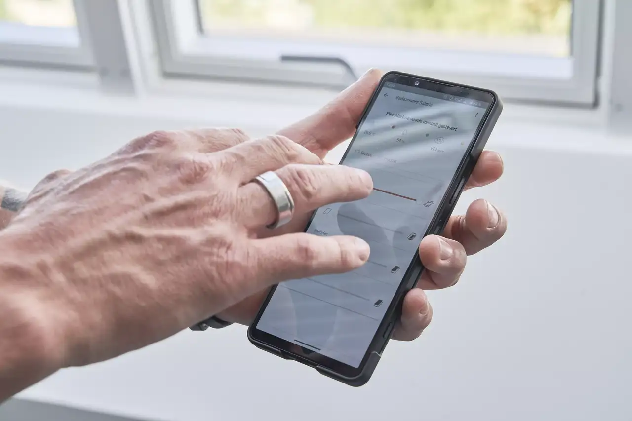Nahaufnahme einer Hand, die eine Smart-Home-App verwendet mit einem VELUX Dachflächenfenster im Hintergrund.