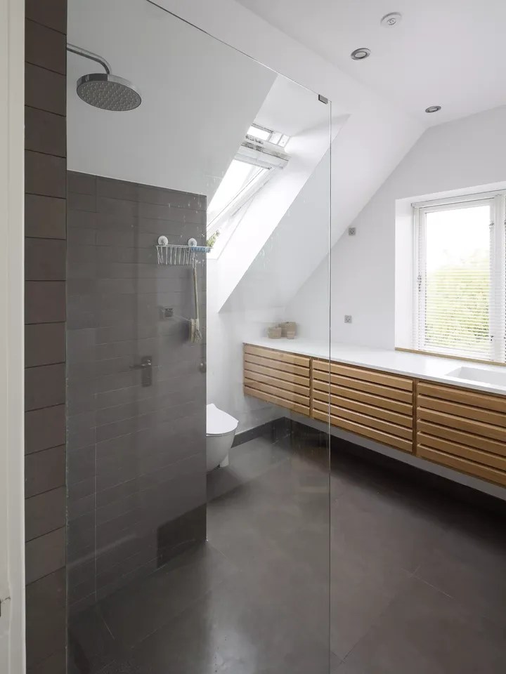 Modernes Badezimmer mit VELUX Dachflächenfenster, Glasdusche und hölzernem Waschtisch.