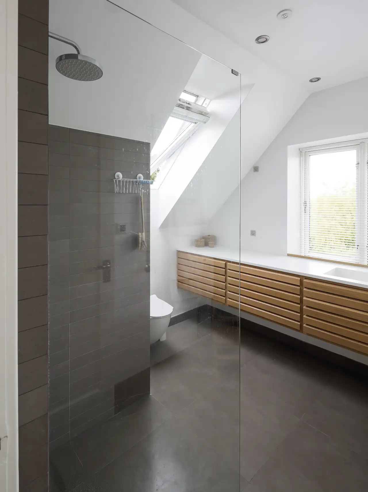 Doccia a pioggia a filo pavimento, con piastrelle nere, di fronte a un grande lavabo con dettagli in legno | Rivista VELUX