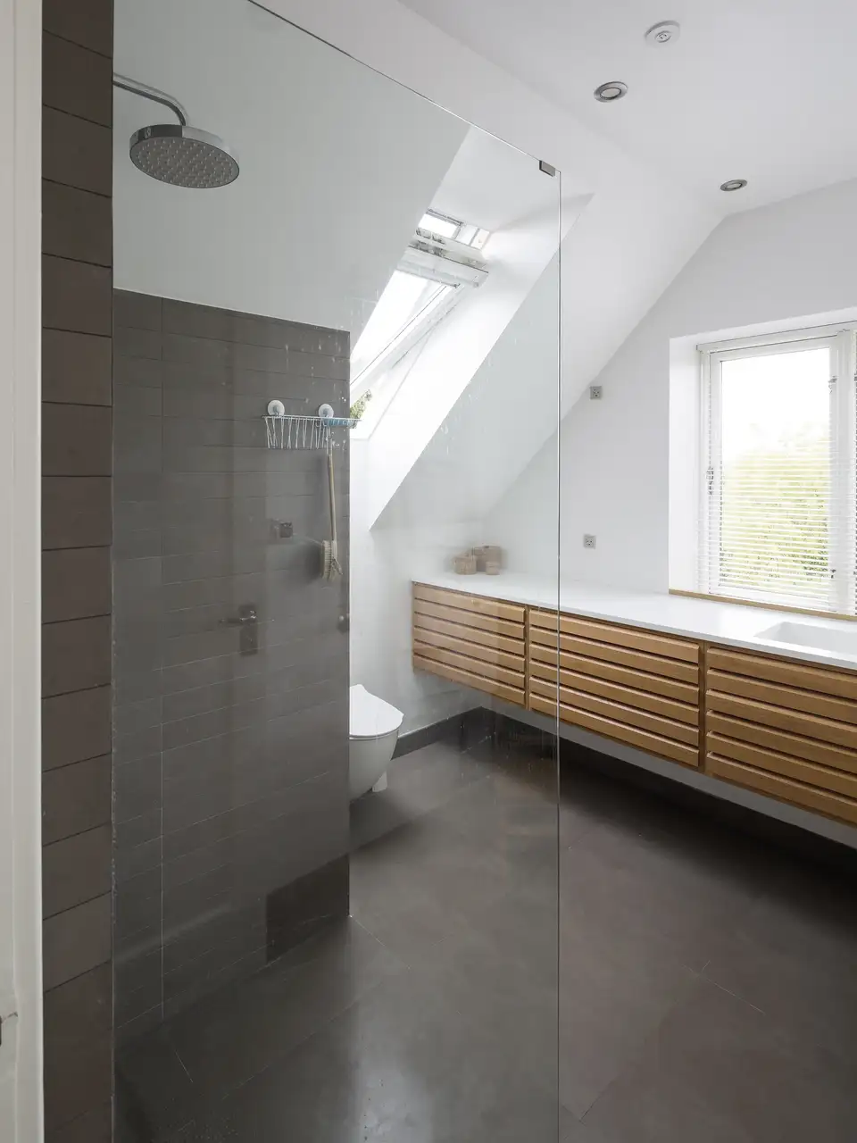 Bagno in mansarda con doccia a filo pavimento e due finestre, una verticale e una per tetti.