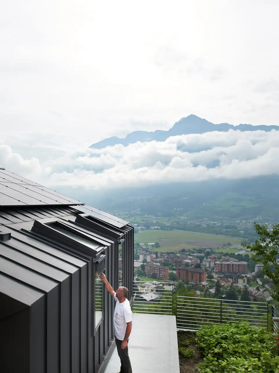Una persona accanto a una finestra per tetti VELUX all’esterno di una casa con vista sulle montagne.