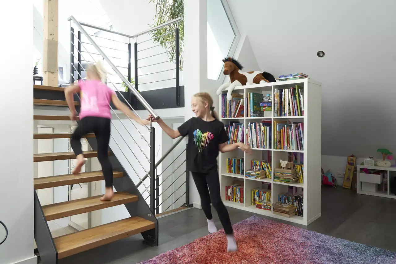 Kinder spielen auf einem modernen Stiegenhaus neben einem Bücherregal unter einem VELUX Dachflächenfenster.
