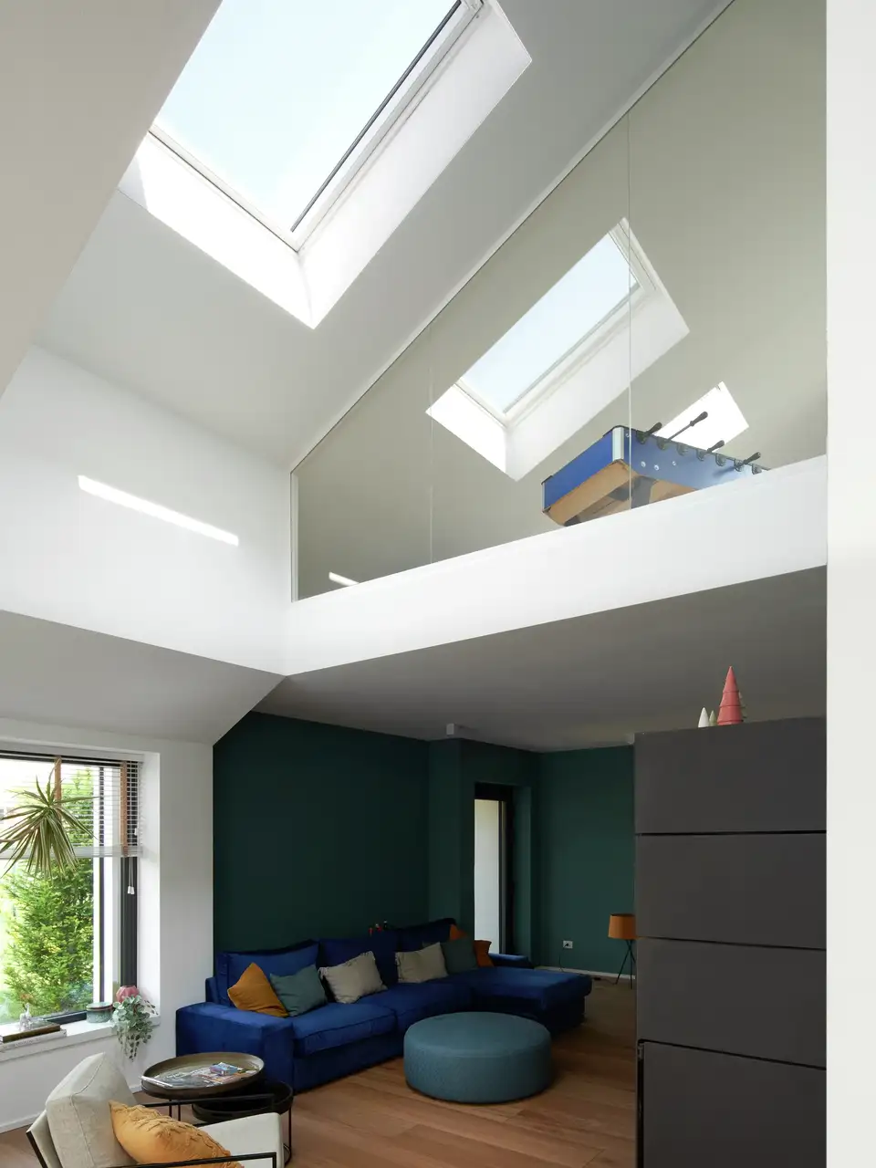 Salon avec plafond très haut équipé de fenêtres de toit et mur bas peint en vert foncé 