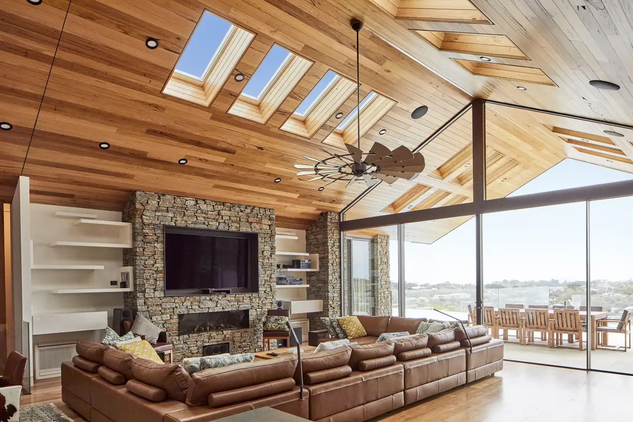 Soggiorno in stile rustico con soffitto in legno, pareti in pietra e arredi in pelle marrone nelle tonalità calde della terra.
