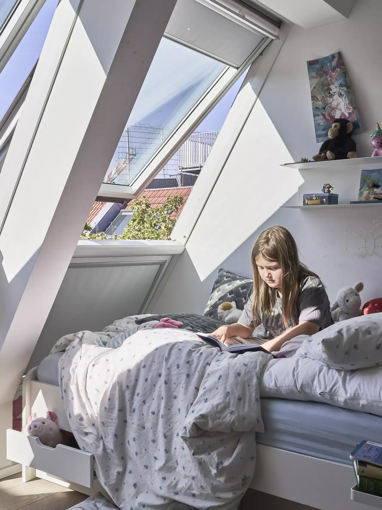 Een buitenpatio met verschillende potplanten en groen. Er is een bakstenen gebouw met grote ramen en een balkon dat uitkijkt op de patio. De ruimte is goed onderhouden en uitnodigend, met een parasol, buitenmeubilair en decoratieve elementen zoals een standbeeld van een dier, mogelijk een kat.