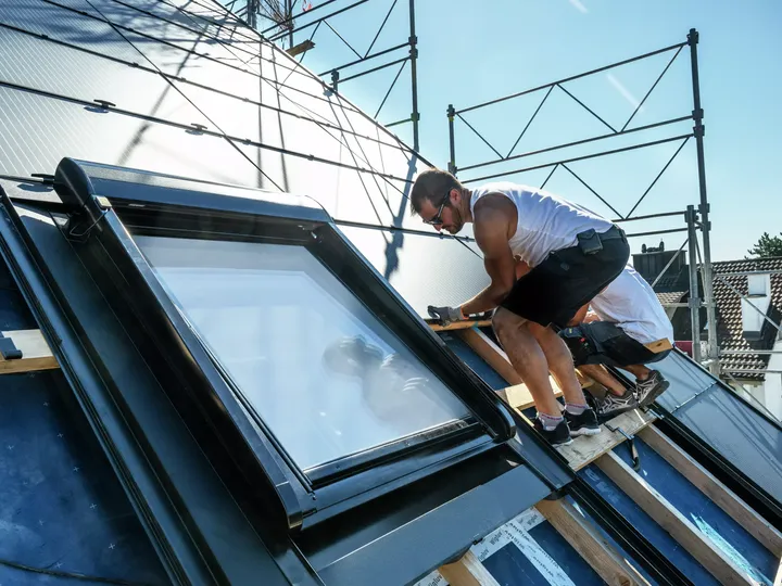 Arbeiter montiert ein VELUX Dachflächenfenster auf dem Dach eines Wohngebäudes.
