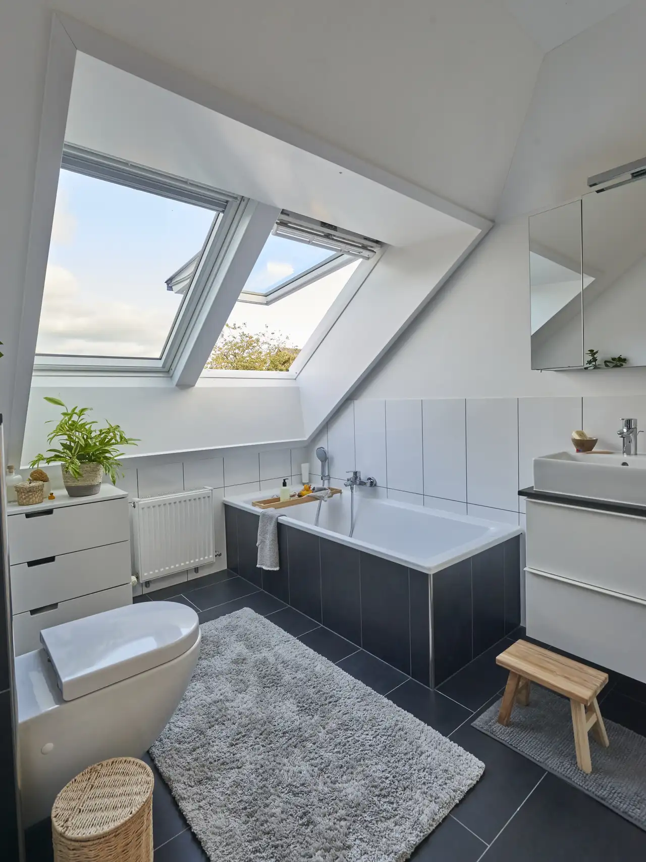 Bagno in mansarda con vasca e mobile contenitore sotto due grandi finestre per tetti.