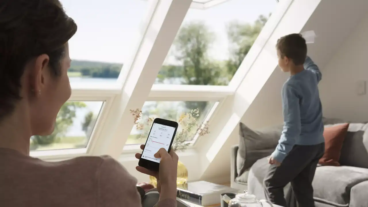 Person verwendet ein Smart-Gerät in einem sonnendurchfluteten Wohnzimmer mit VELUX Dachflächenfenster.