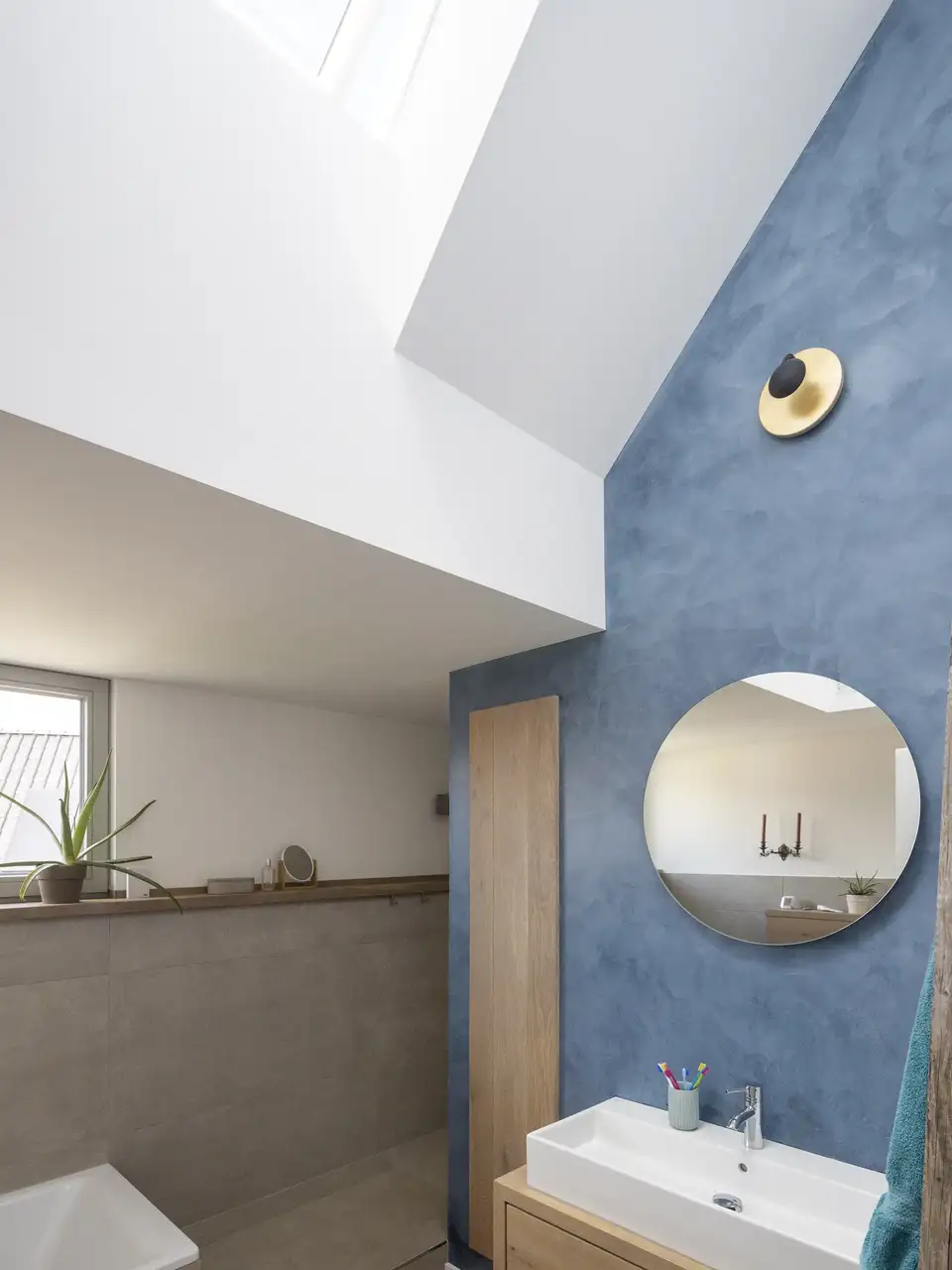 Salle de bains mansardée avec fenêtres de toit VELUX, mur bleu intense et mobilier en bois clair 
