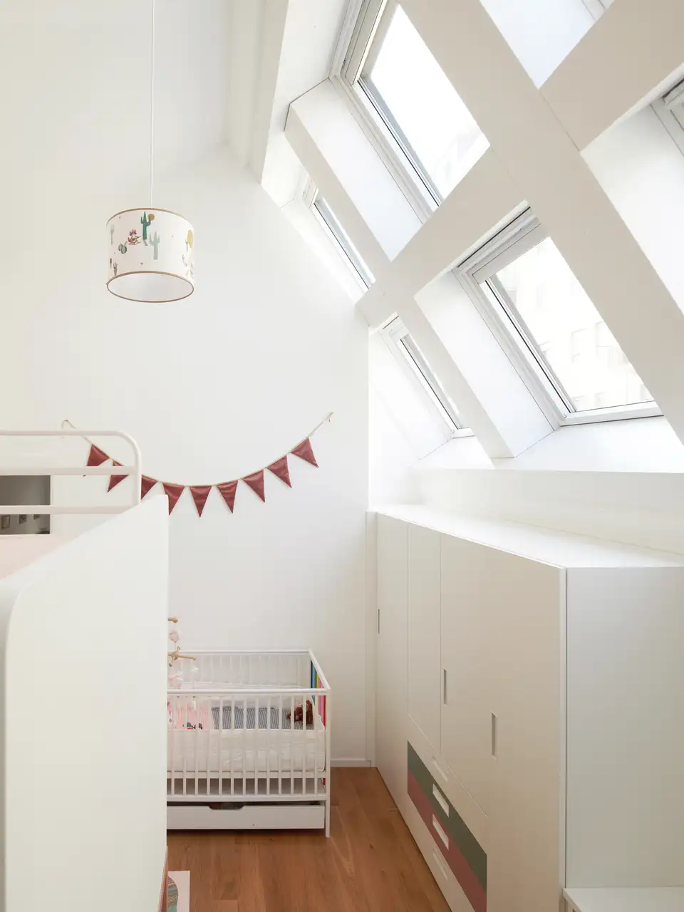 Renovatie van een kinderkamer op zolder met schuin dak en VELUX dakvensters, kinderbedje en stapelbed."