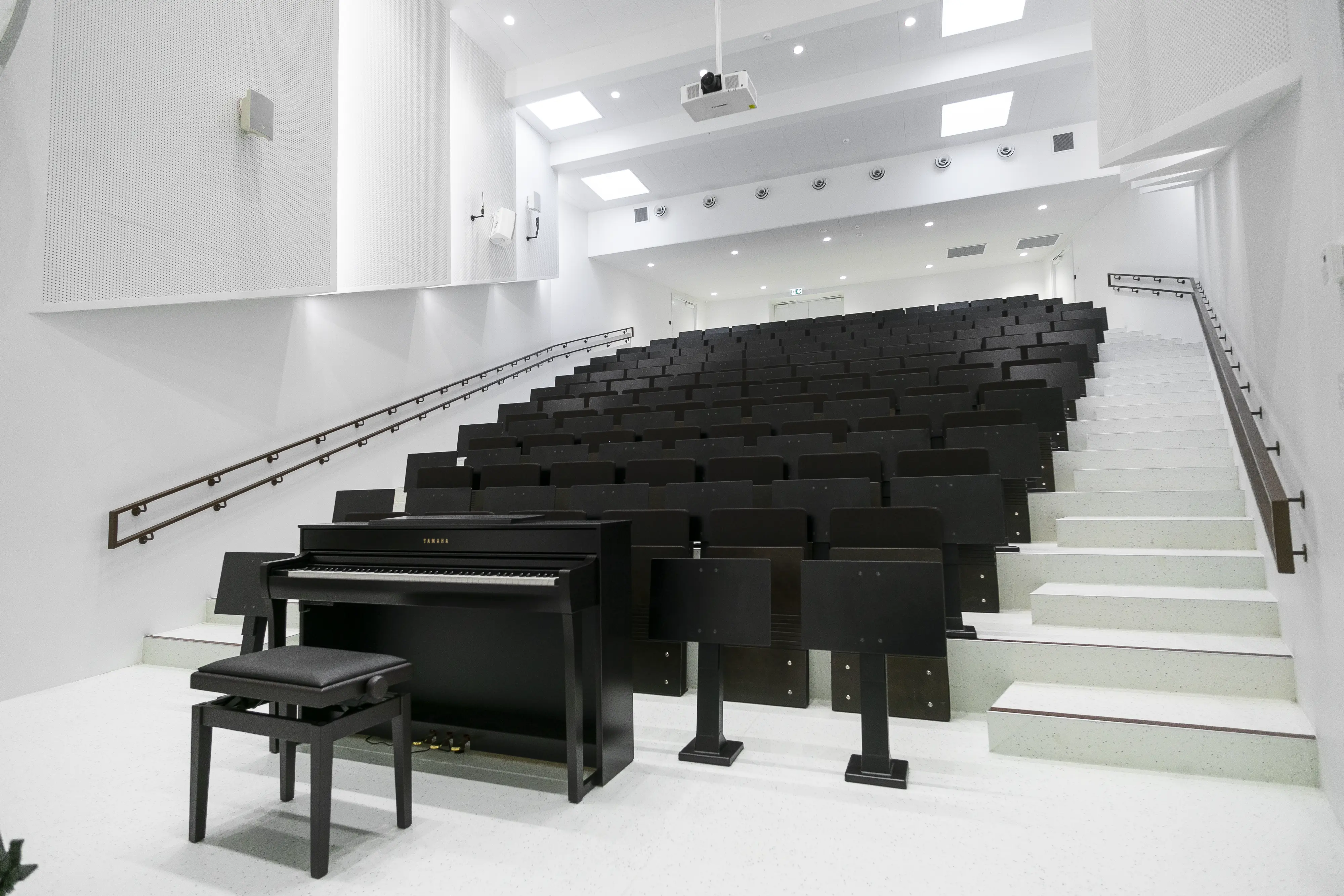 Sala wykładowa z wielopoziomowymi siedzeniami i czarnym fortepianem, nowoczesny design.