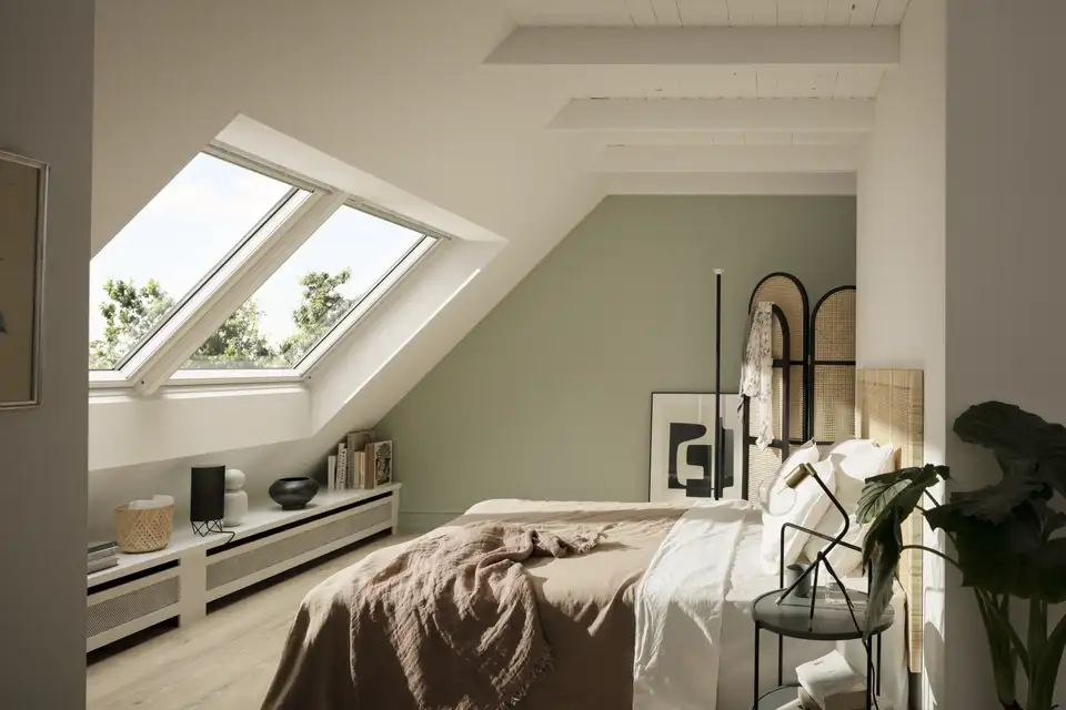 Camera da letto con parete d’accento verde salvia e finestre per tetti che portano luce naturale