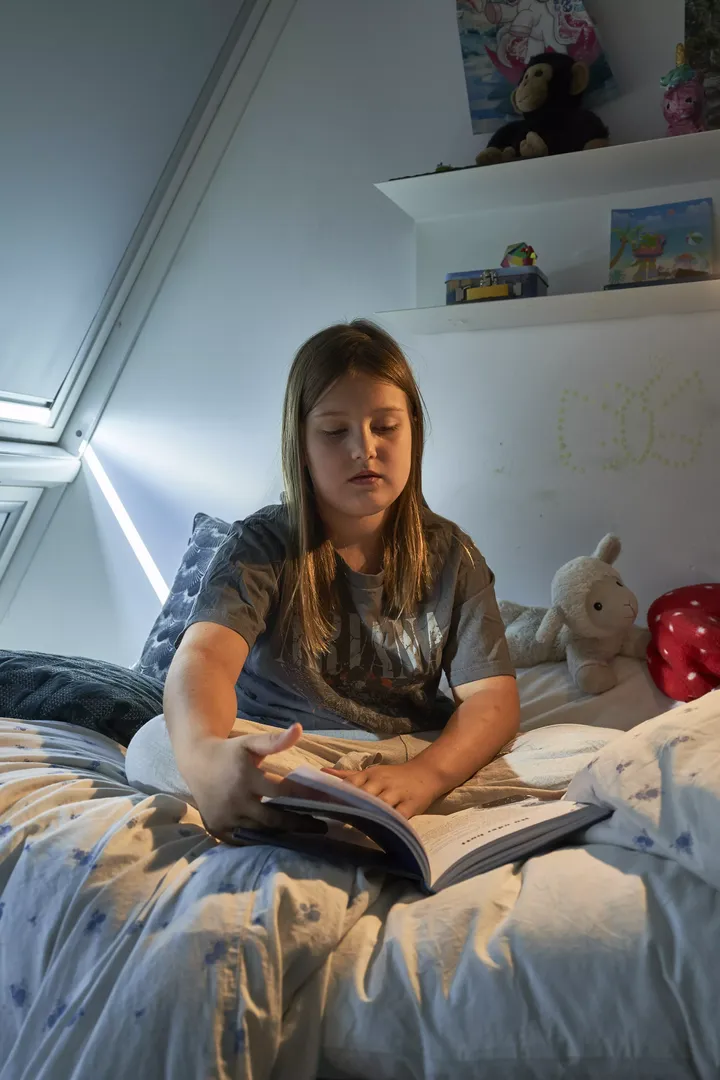 Teenager liest in einem sonnendurchfluteten Raum mit einem VELUX Dachflächenfenster und gemütlicher Bettwäsche.