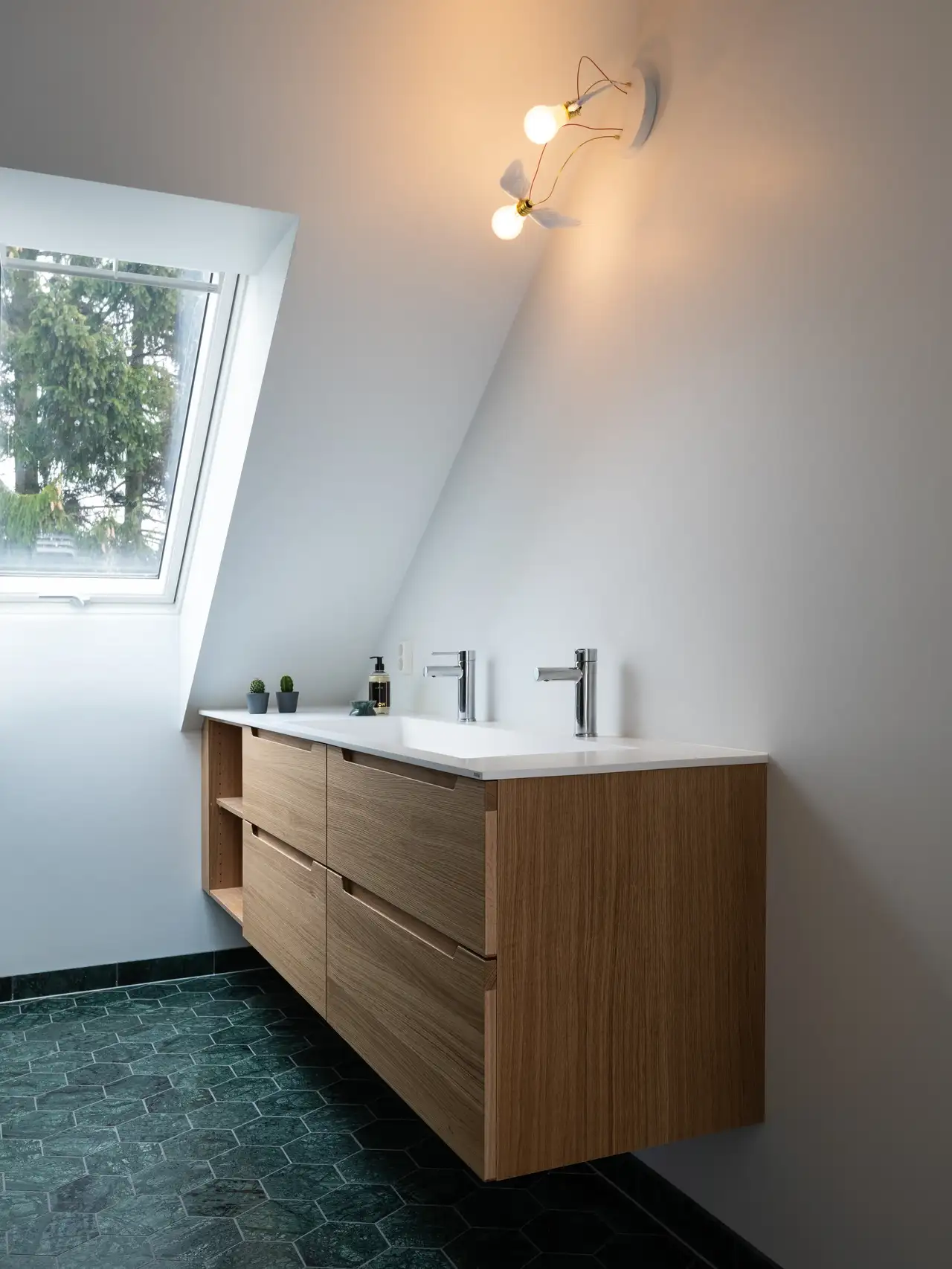 Salle de bain avec meuble en bois, double vasque, fenêtre de toit et lampes à faible consommation. 